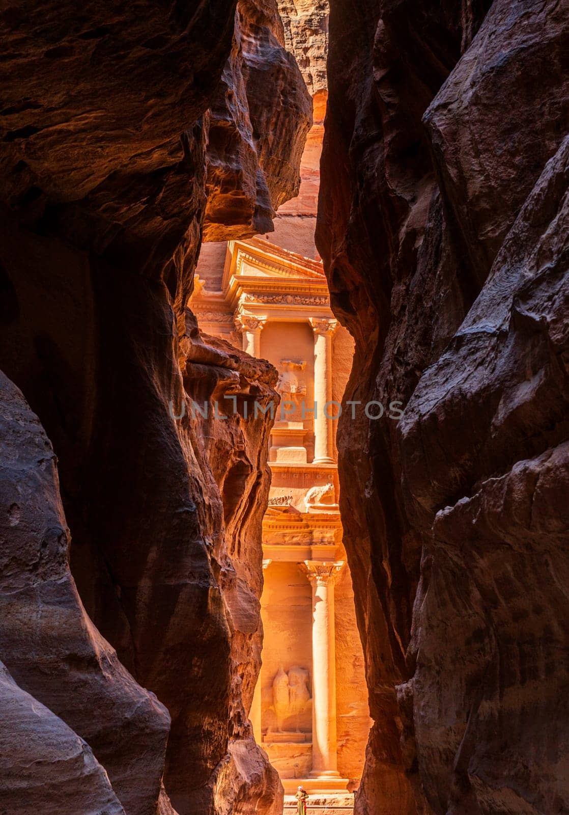 The carved facade of the Treasury building or Al-Khazneh in the ancient city of Petra in Jordan seen through narrow Siq gorge