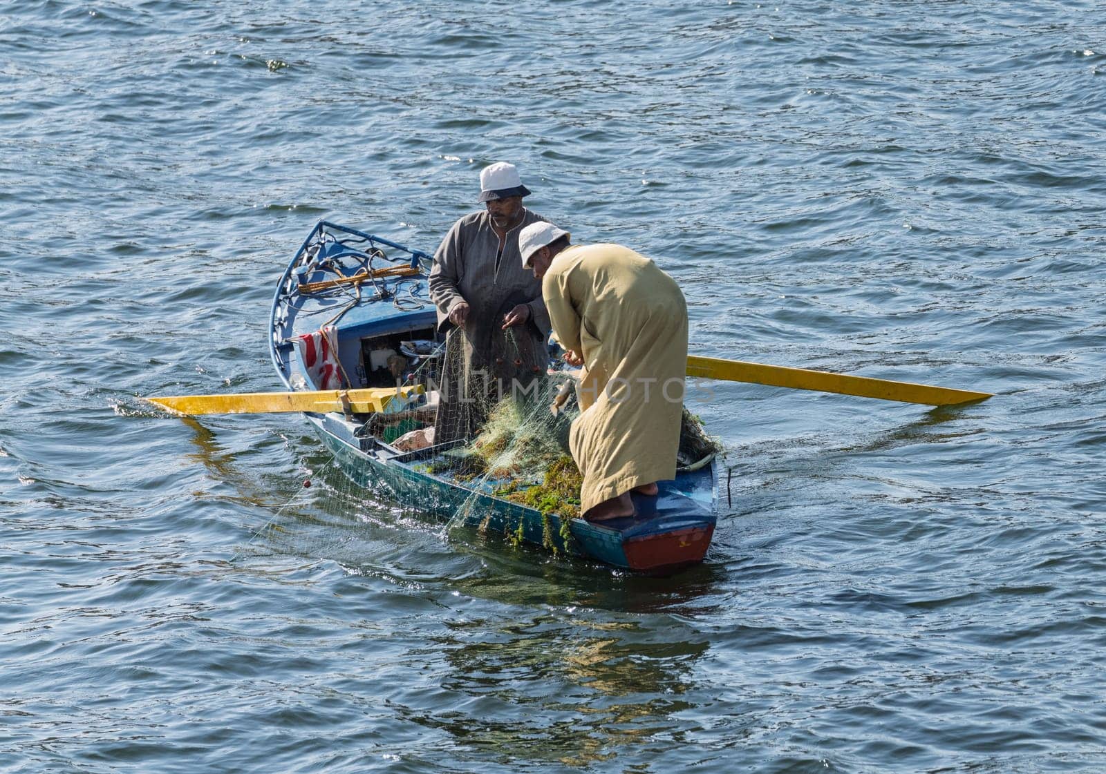 Two men in small wooden fishing boat with fish caught in their net from the river Nile