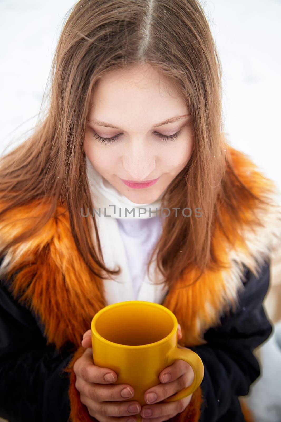 Woman in winter attire holds a yellow mug, enjoying a snowy walk with her fluffy Pomeranian dog nearby.