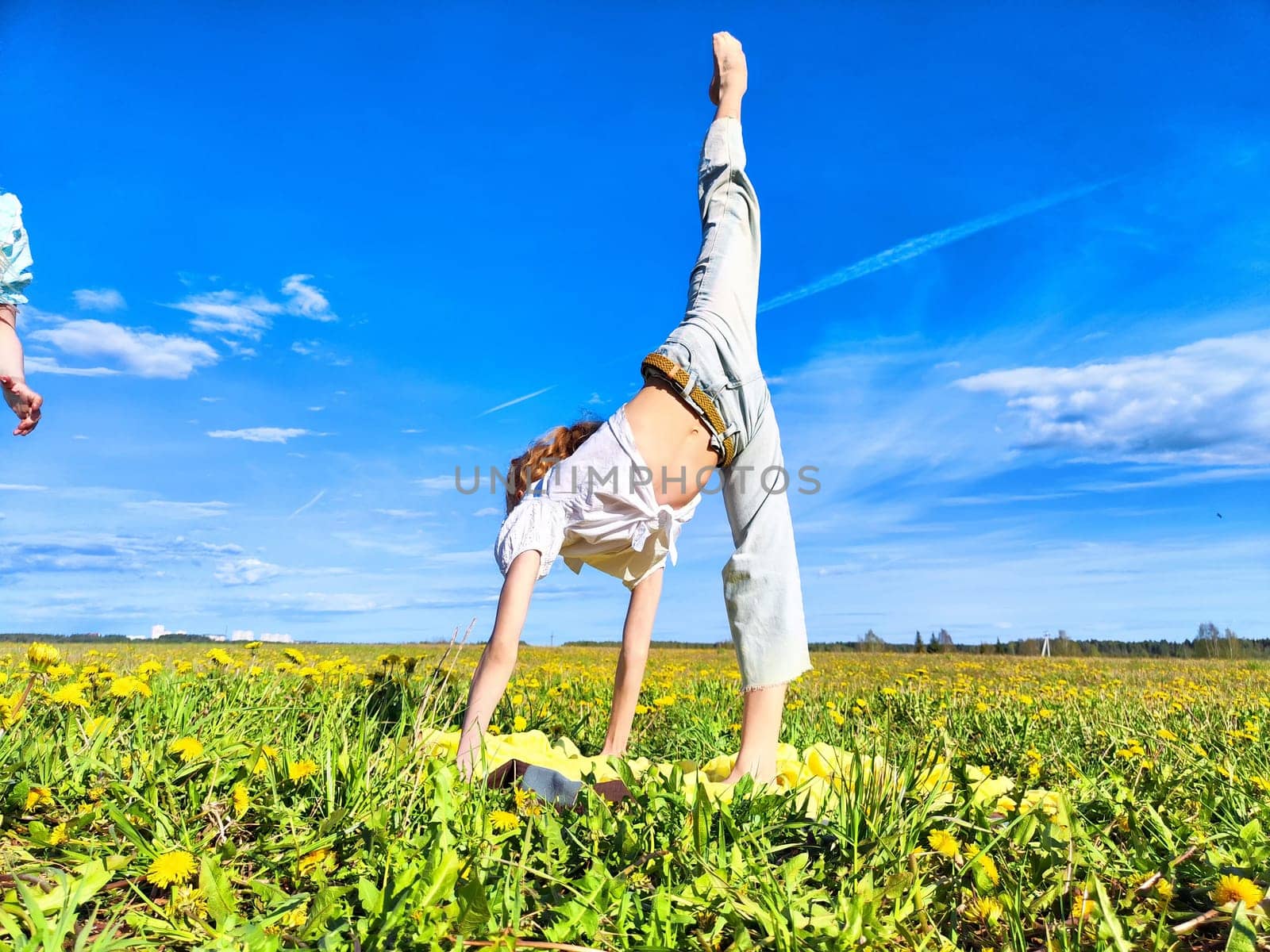 A child is performing a handstand in a vibrant meadow surrounded by blooming yellow flowers on a bright sunny day.