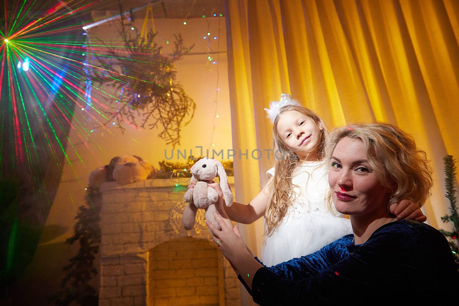 A mother and daughter enjoy the festive atmosphere, holding a stuffed animal while surrounded by holiday lights and decorations.