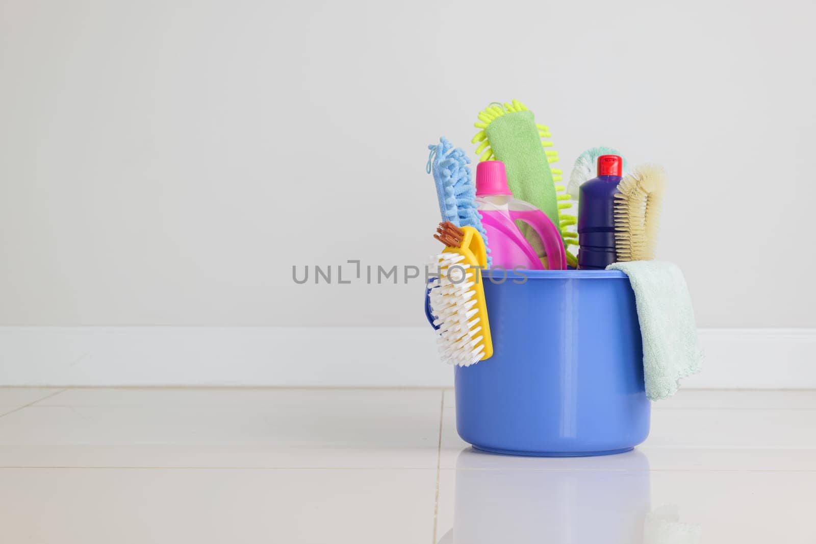 Cleaning routine essentials. blue plastic bucket filled with detergent bottles, brushes, and other cleaning supplies sits on the floor in the living room, prepared for housekeeping and daily housework