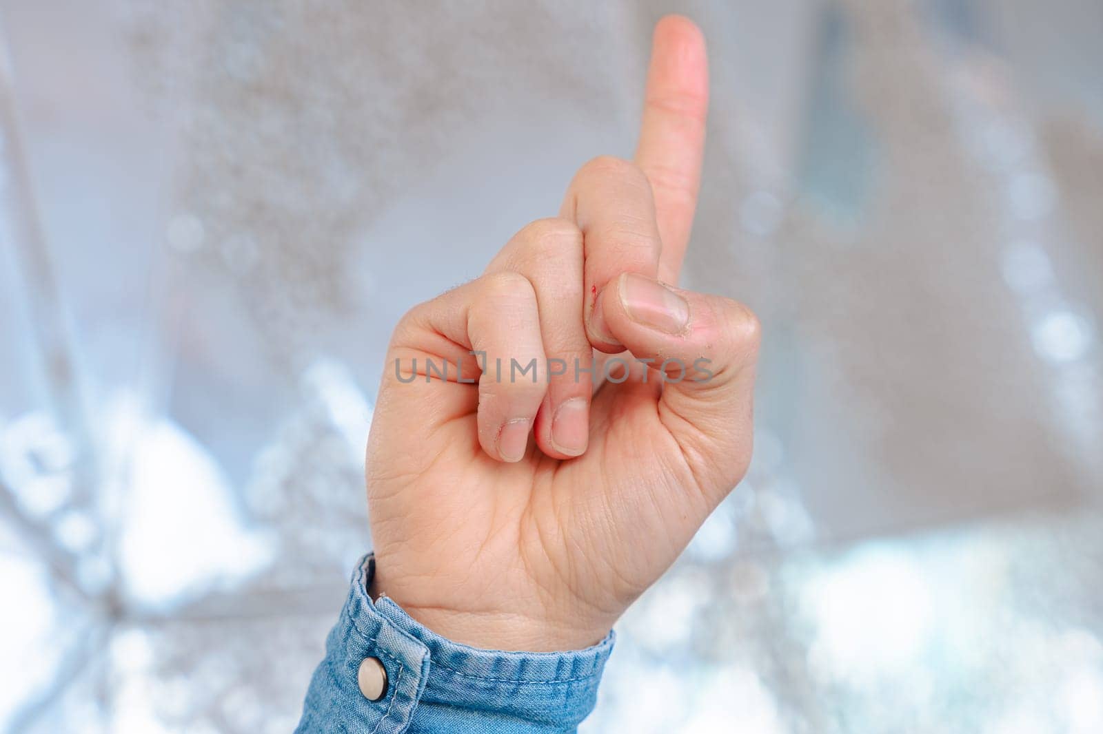 close-up image of a human hand wearing a denim shirt, raising a single finger upward in a pointing gesture, with a soft reflective background, symbolizing direction, focus, or instruction.