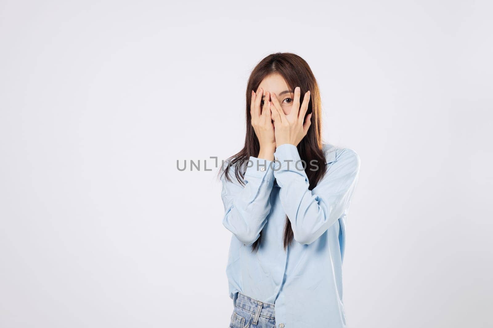 Woman hides in fear, afraid woman covers her face using both hands, reacting to something scary with expressive eyes, on a clean white studio isolated background.