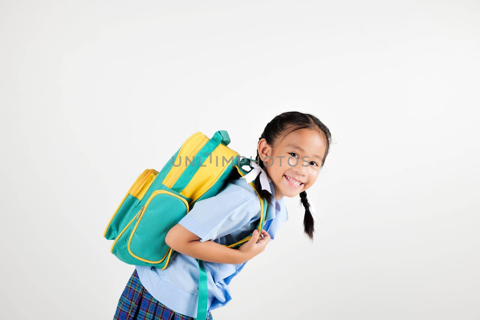 Portrait smile Asian little girl kindergarten holding a green and yellow backpack posing studio isolated white background, happy cute woman kid wear school uniform plaid skirt, back to school concept