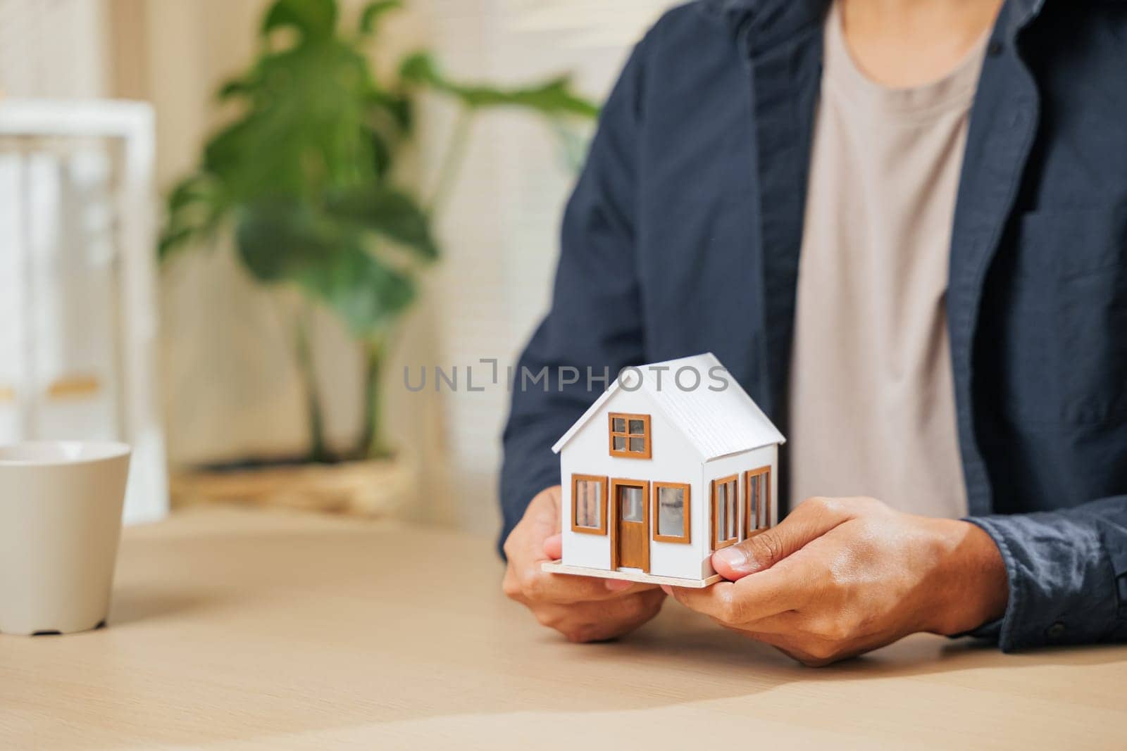 Close-up of a real estate agent hand holding a small house model, symbolizing property, home loan, and finance concepts. Represents the role of an agent in real estate, housing, and loan planning.