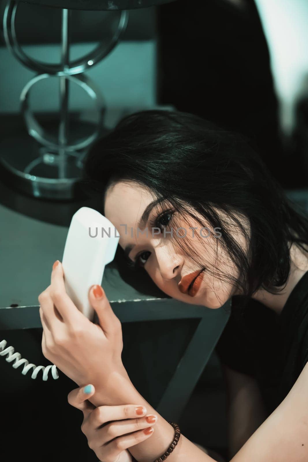 Asian Woman staring and holding the white phone in her hand while wearing a black dress and bracelet in her hand in the bedroom