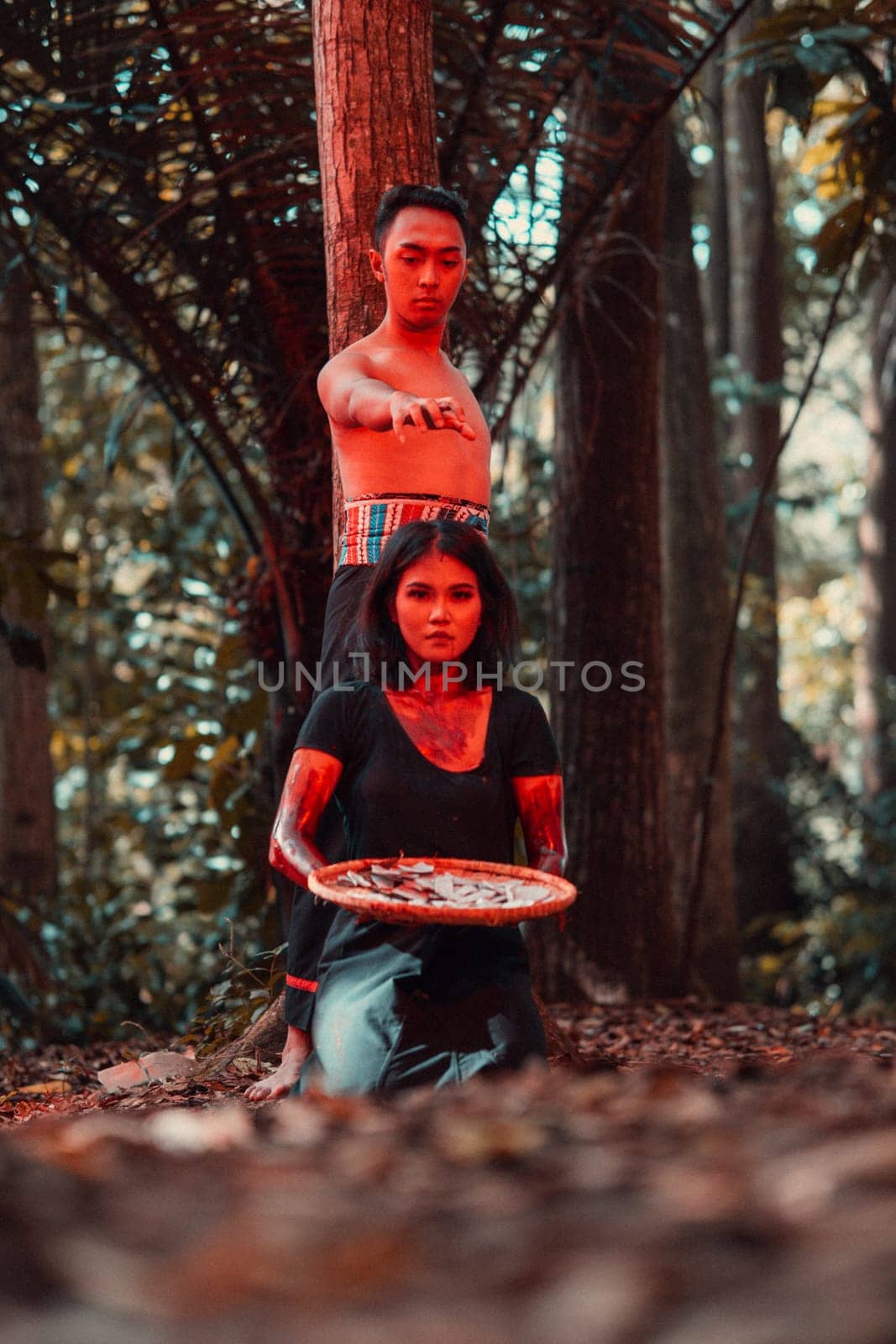an Asian woman and man were standing in front of a tree while hunting an animal in the middle of the forest until they were covered in blood in the afternoon