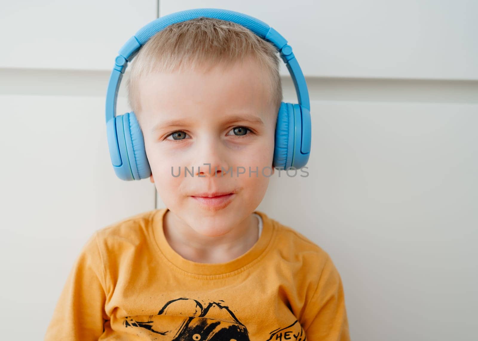 portrait of a 4-year-old boy in an orange sweatshirt and blue headphones listening to music. High quality photo