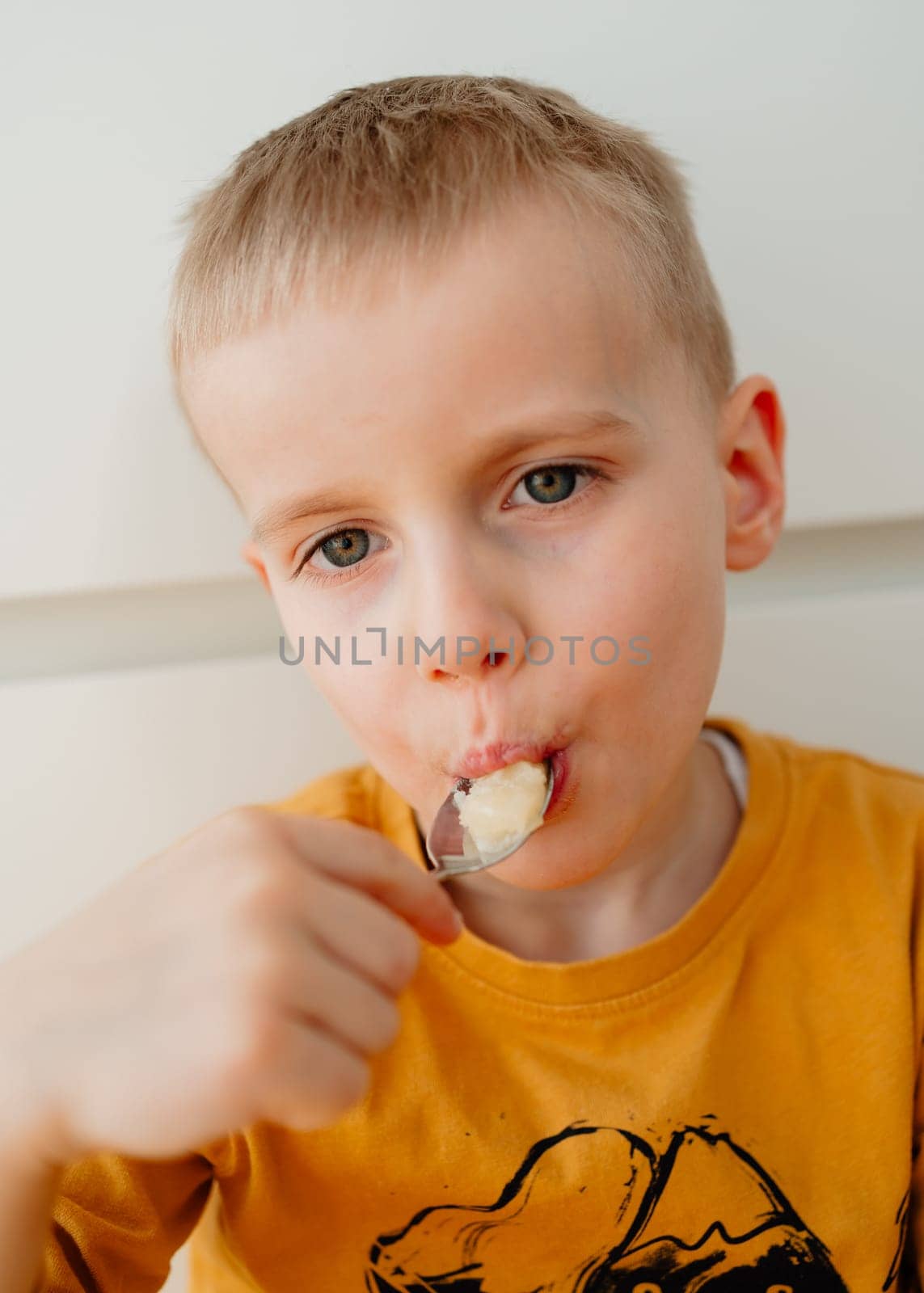a 4-year-old blond boy eats honey from a spoon with his mouth open. High quality photo