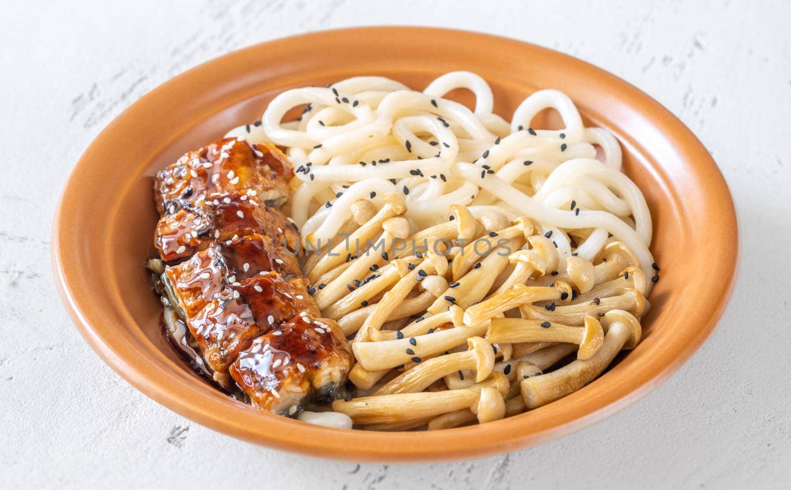 A hearty udon bowl topped with eel, mushrooms, and toasted sesame garnish