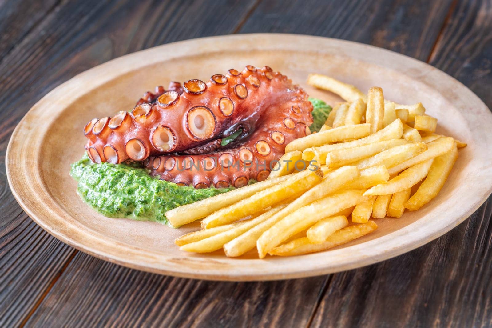 Roasted octopus tentacles served with creamy spinach and golden fries, rustic plating style