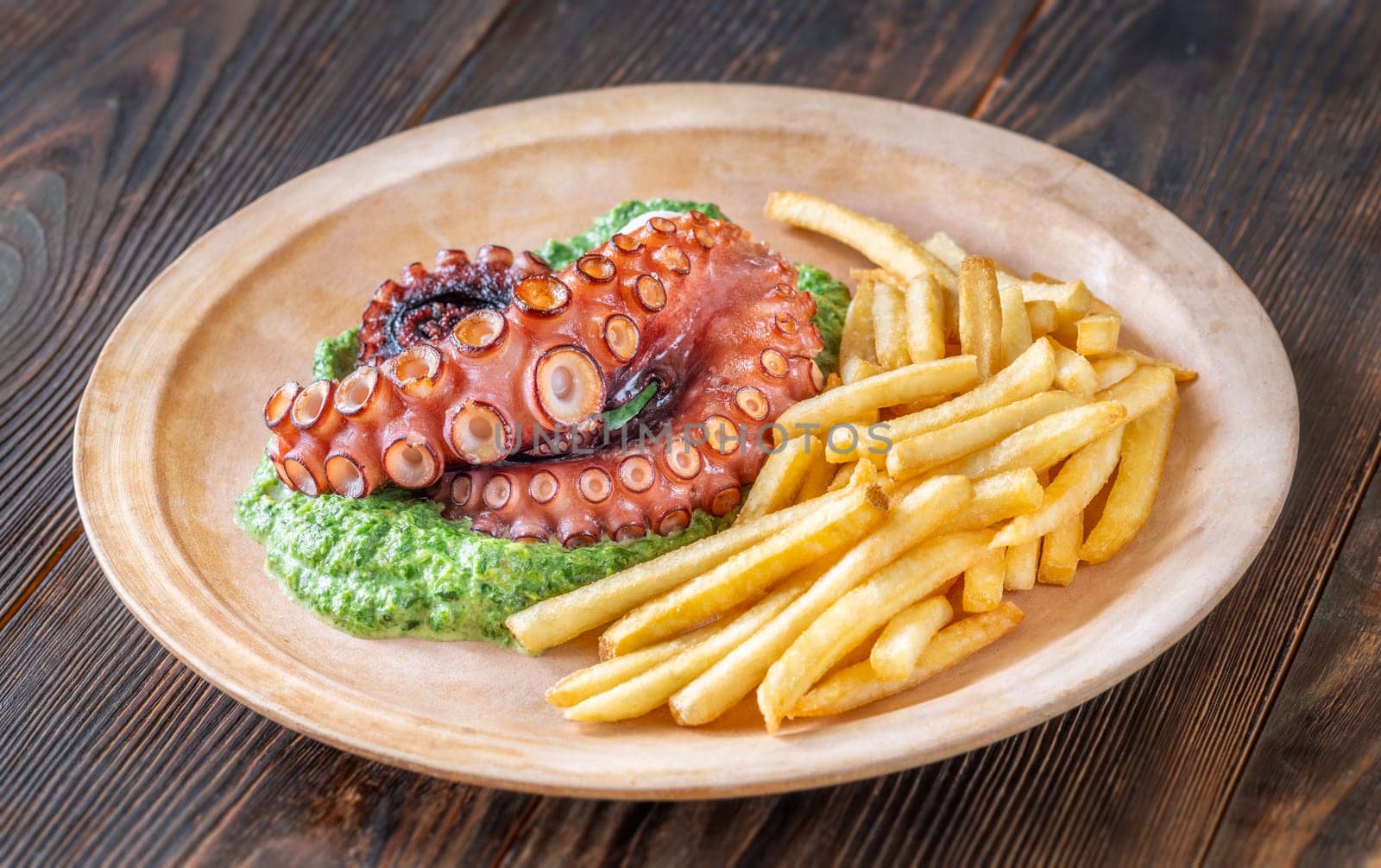 Roasted octopus tentacles served with creamy spinach and golden fries, rustic plating style