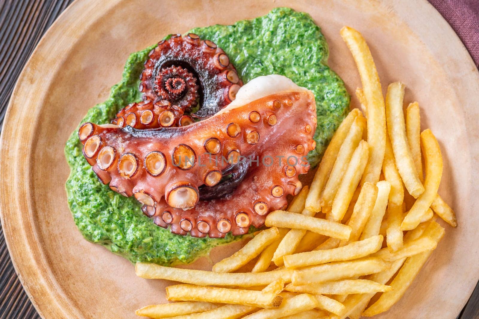 Roasted octopus tentacles served with creamy spinach and golden fries, rustic plating style