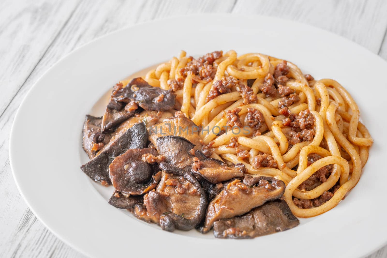 White plate of thick udon with beef, and mushroom topping