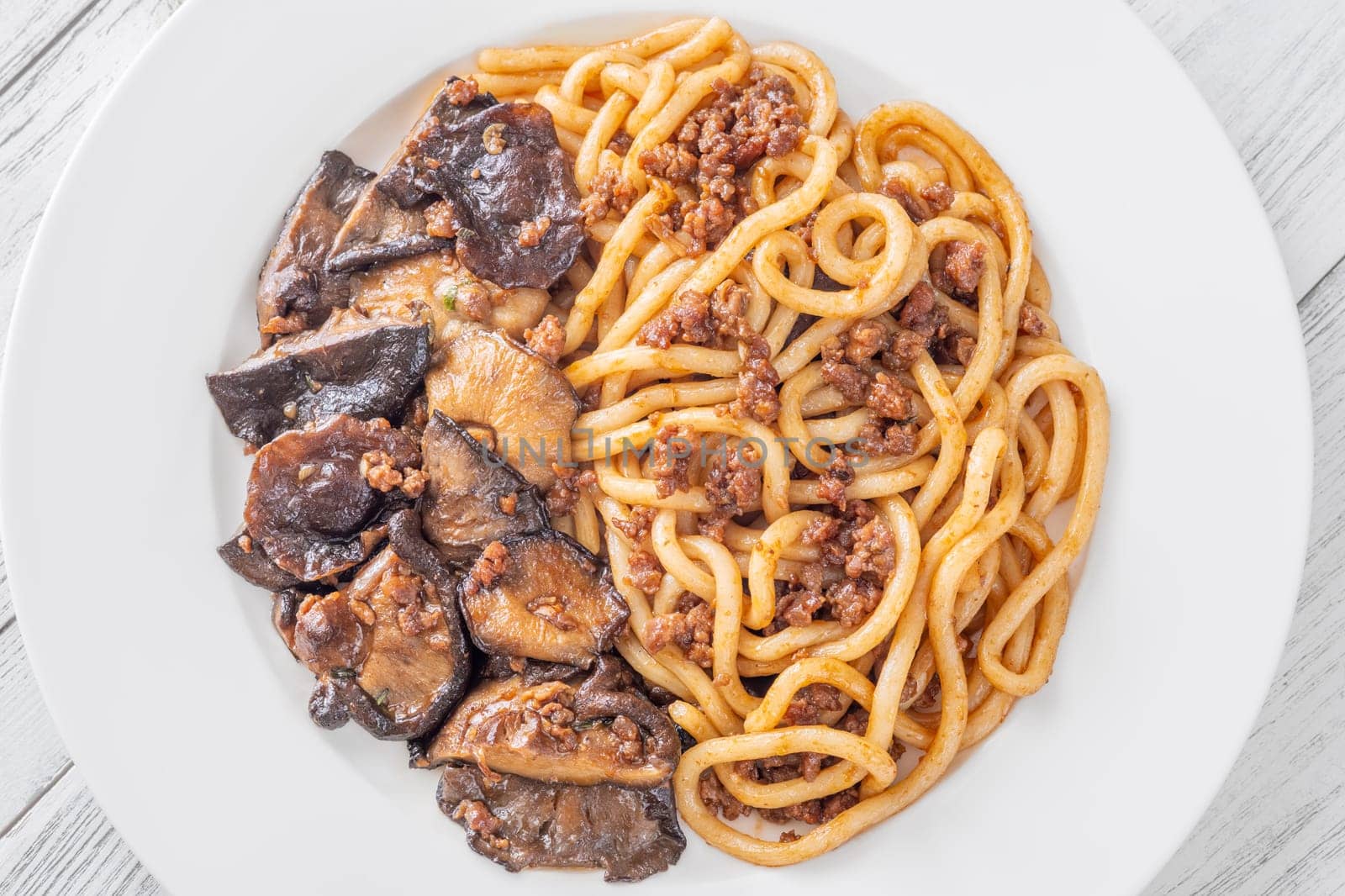 White plate of thick udon with beef, and mushroom topping