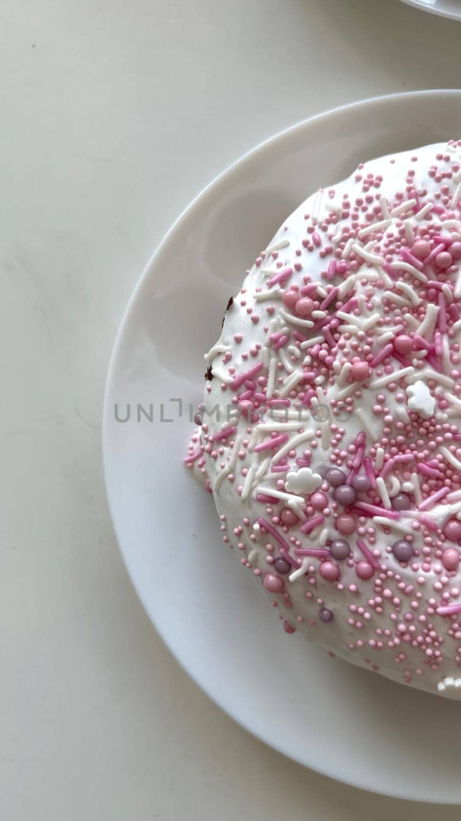 Round cake adorned with pink sprinkles and creamy icing on a white plate, presenting a delightful dessert ideal for celebrations and special occasions, a sweet treat that brings joy