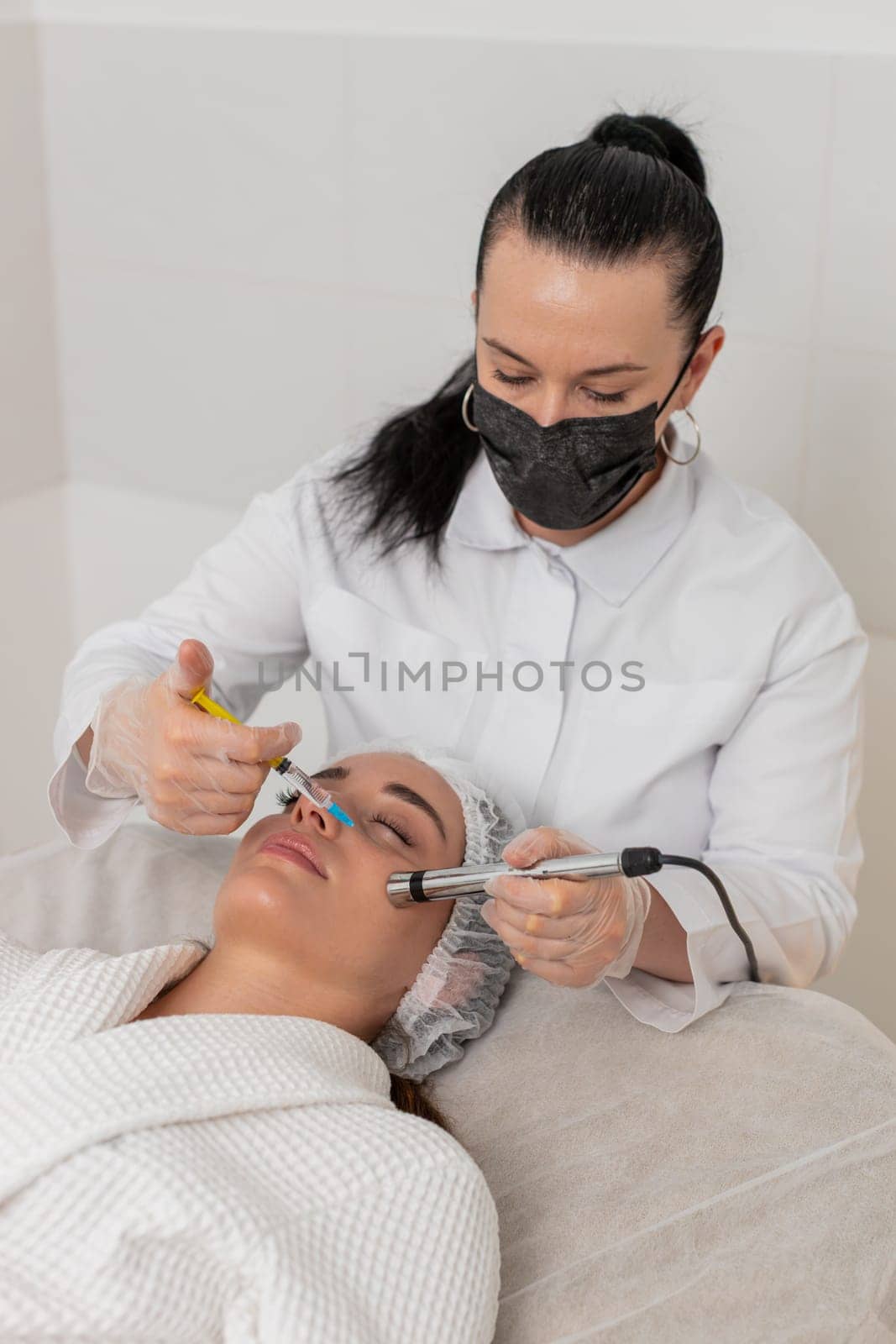 Caucasian woman girl receives non-invasive face rejuvenation during electroporation procedure. Cosmetologist applies advanced therapy in beauty clinic to improve skin tone and reduce signs of aging.