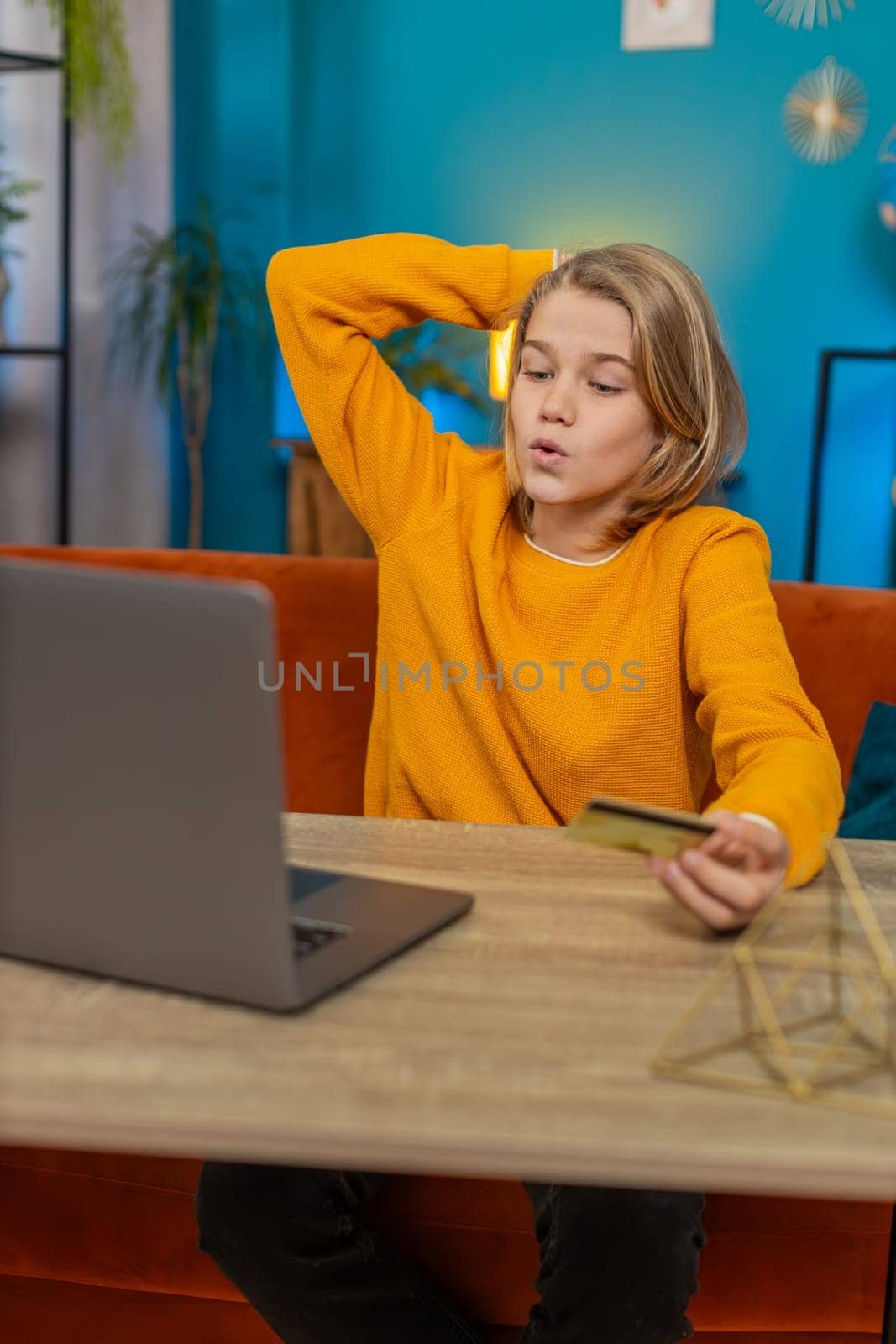 Caucasian teenager boy making an online purchase on laptop at home. Entering credit card information, clicking Order for new game item while sitting on couch by table, feeling satisfied with purchase