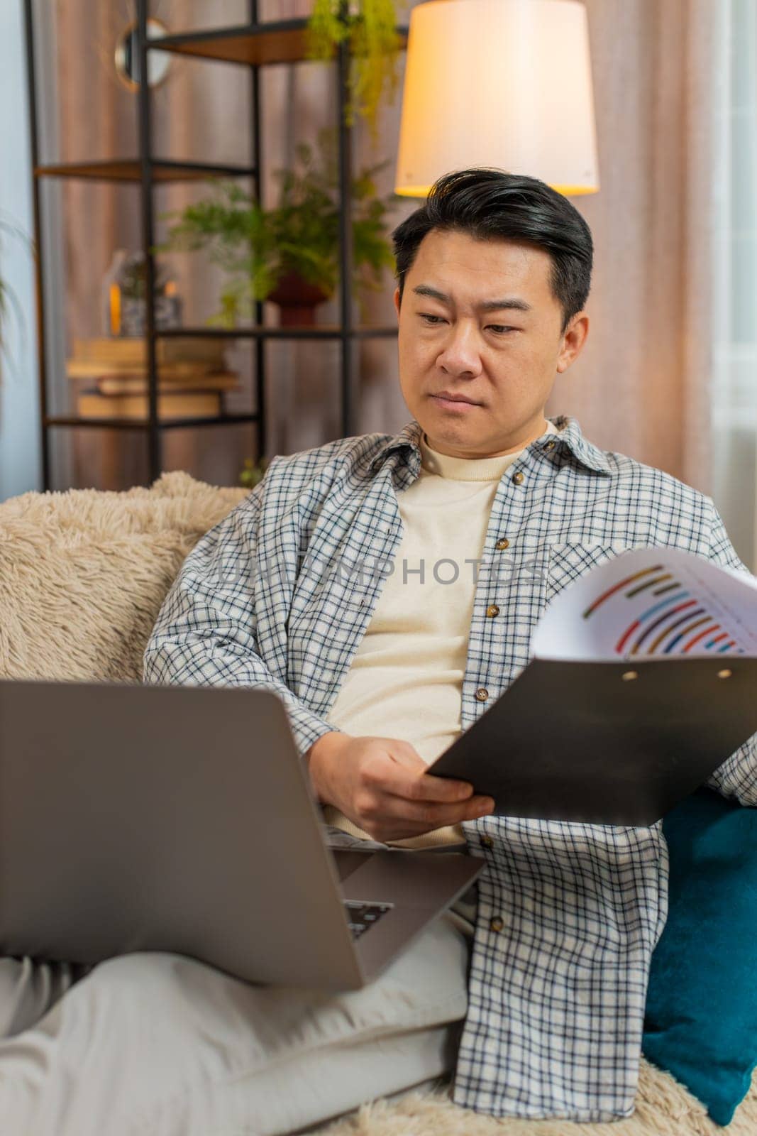 Stressed man freelancer feeling worried about financial problem doing paperwork sitting on sofa in living room. Tired Middle Eastern male frustrated thinking of money debt, budget loss, bankruptcy.