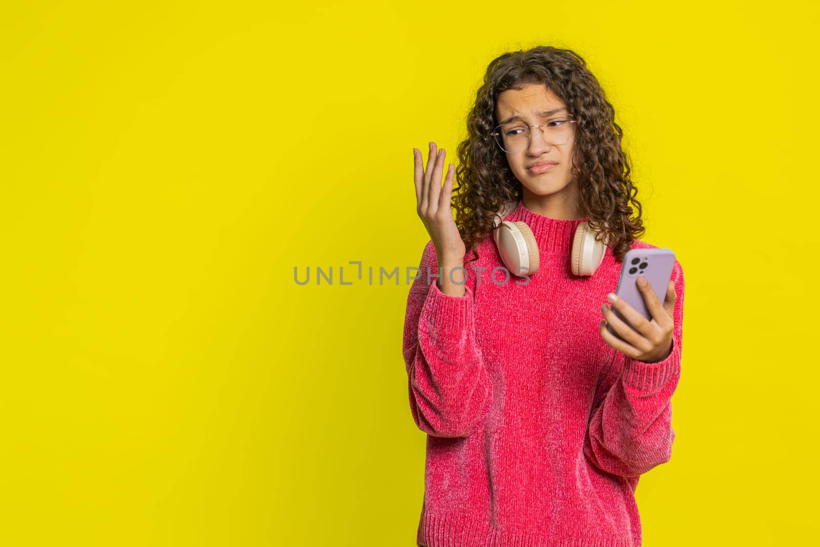 Upset sad Caucasian girl use smartphone typing browsing, play game, loses surprised by sudden lottery results bad fortune loss fail unlucky news. Unhappy teenager child isolated on yellow background