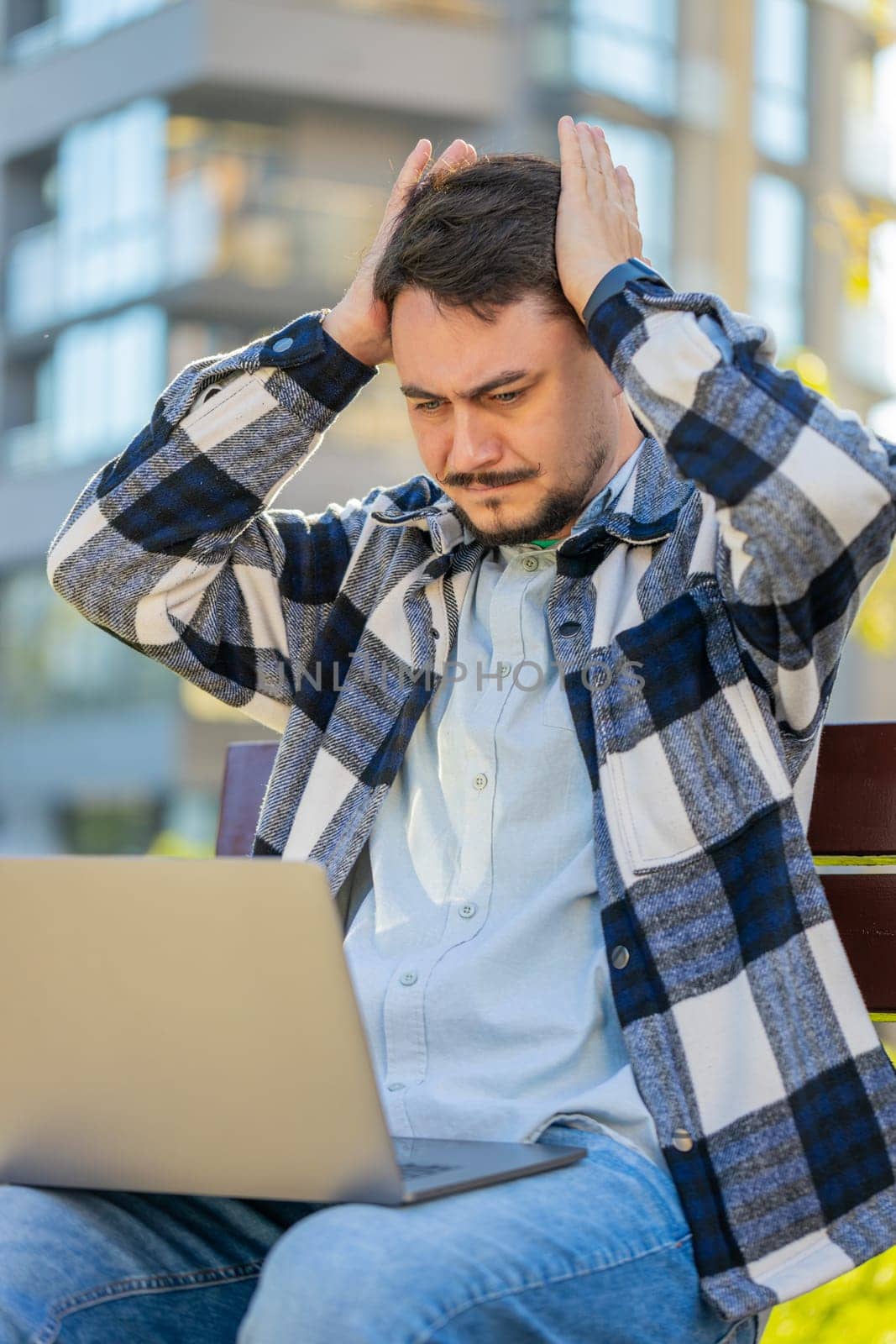 Sad mature man tourist using laptop computer typing browsing, loses becoming surprised sudden lottery results, bad news, fortune loss, fail. Angry guy sitting on bench downtown. Town lifestyles.