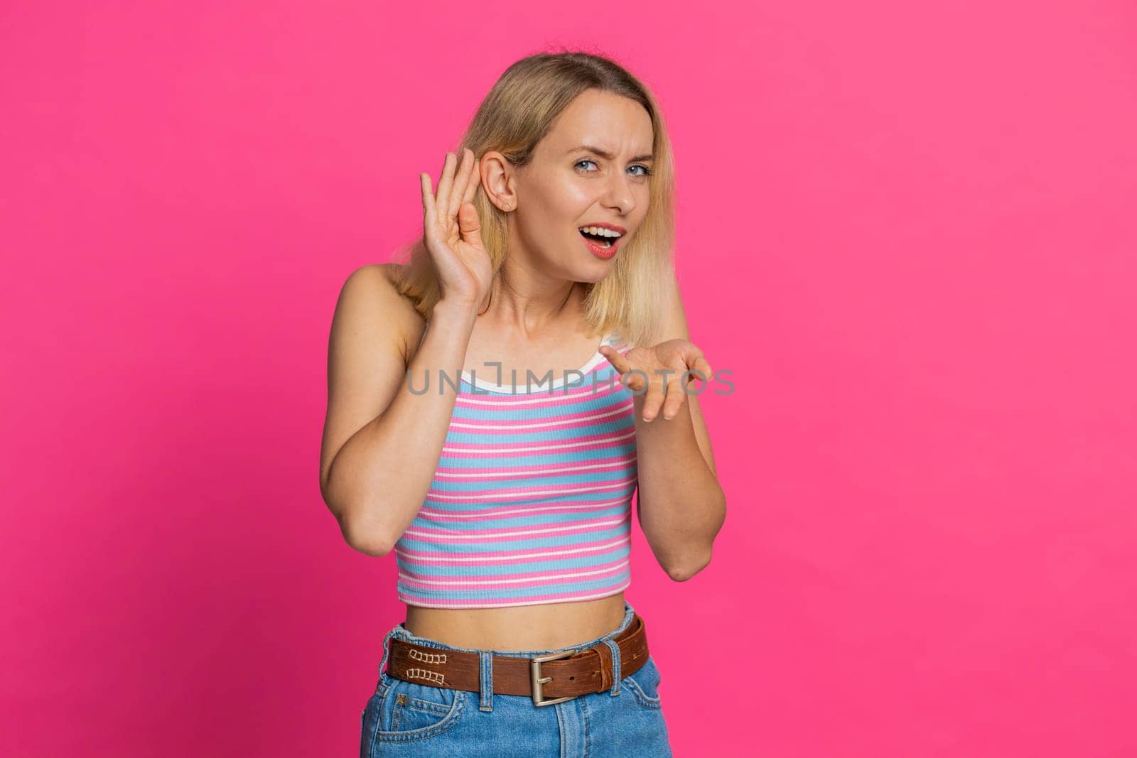 I cant hear you. What. Caucasian woman trying hear you looking confused and frowning keeping arm near ear for louder voice asking to repeat, to hear information deafness. Young girl on pink background