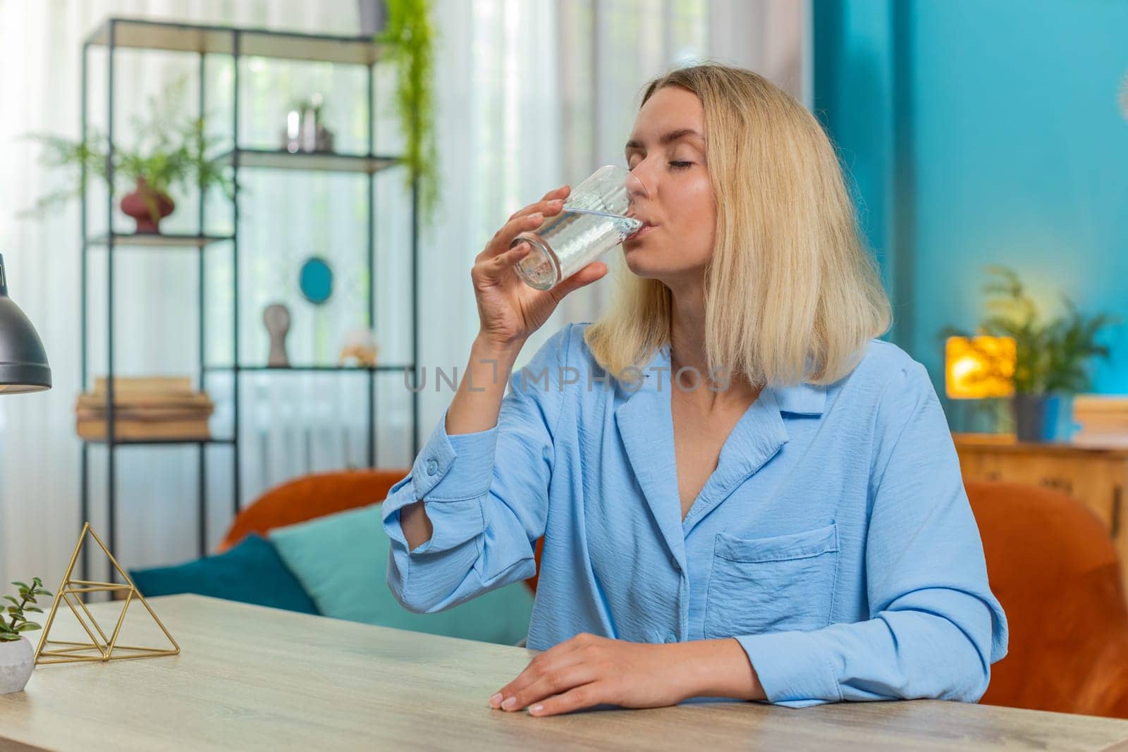 Thirsty young woman hold glass of natural filtered aqua makes sips drinking still water preventing dehydration. Water after reverse osmosis filter. Blond girl with good life habits healthy lifestyles.