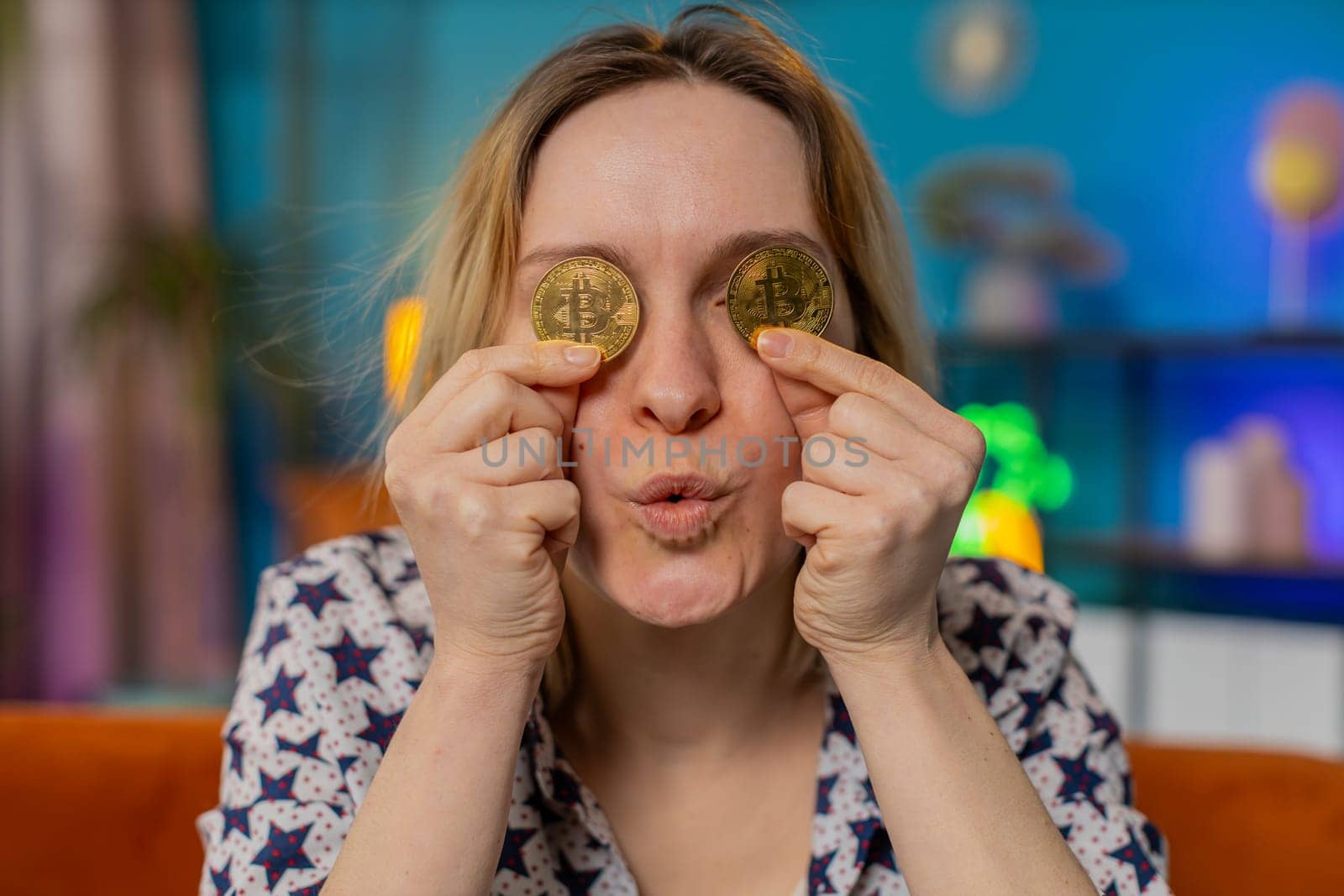 Amazed happy woman holds two gold BTC coins at home successful developer programmer. Girl stock trader earning bitcoins after online monitoring trading operations. Increasing wealth covering eyes