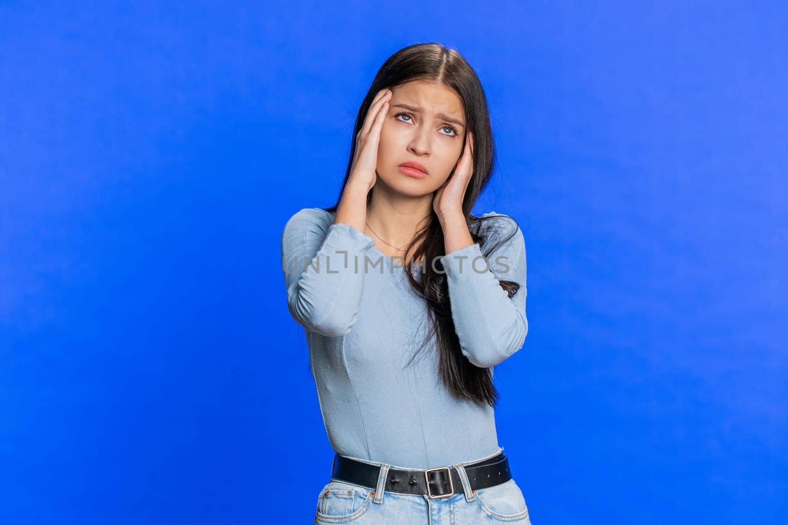 Attractive exhausted young woman girl rubbing temples to cure headache problem, suffering from tension, migraine, stress, grimacing in pain, high blood pressure isolated alone on blue wall background
