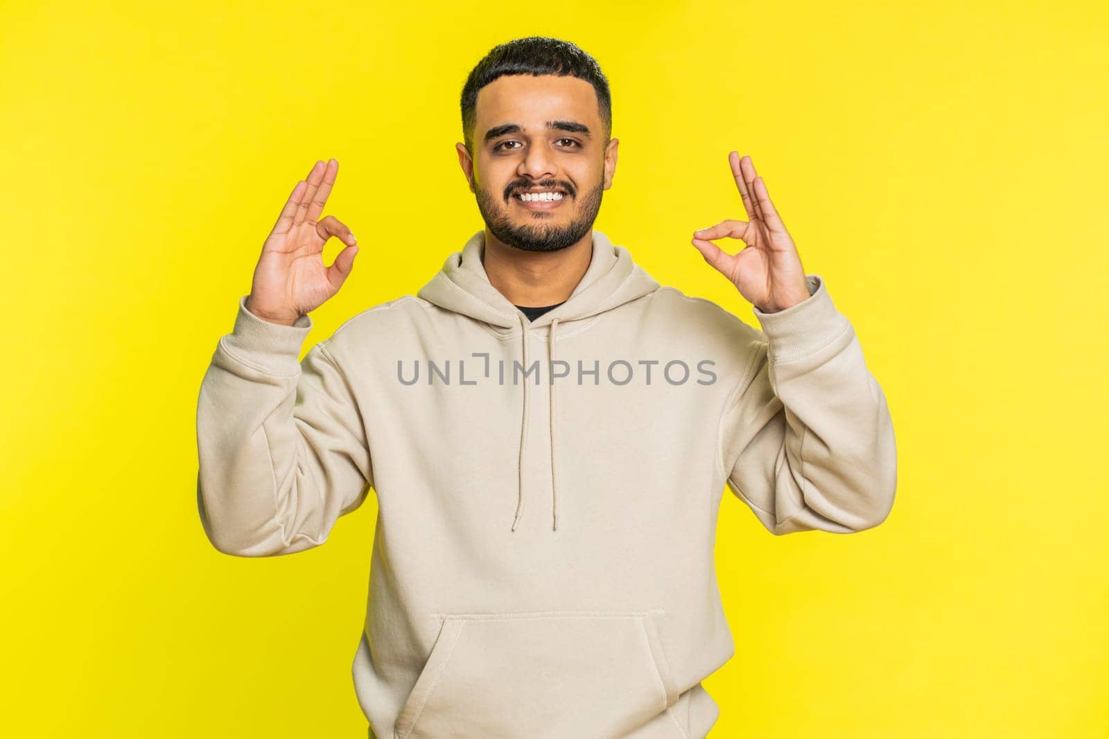 Keep calm down, relax, rest. Concentrated happy Indian man meditating breathes deeply with mudra yoga gesture, eyes closed, peaceful mind taking a break. Arabian Hindu guy on yellow background indoors