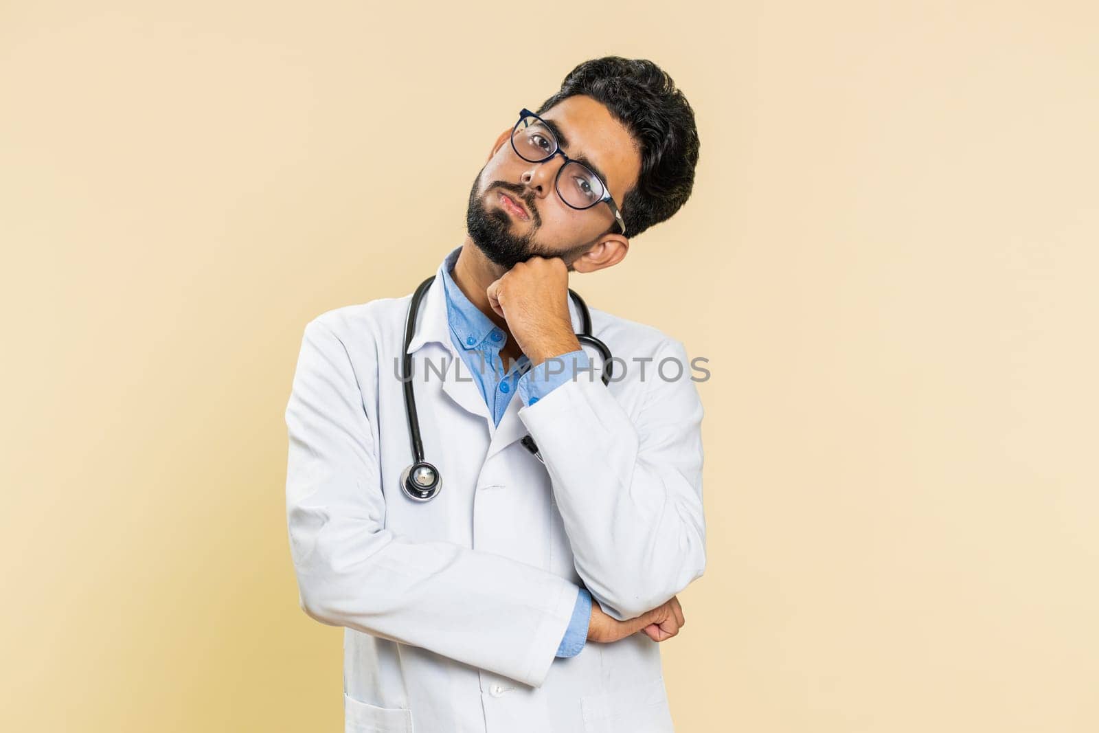 Sad Indian young doctor cardiologist man tired bored exhausted indifferent expression, not interested in communication talk, displeasure. Arabian apothecary pharmacy guy isolated on beige background
