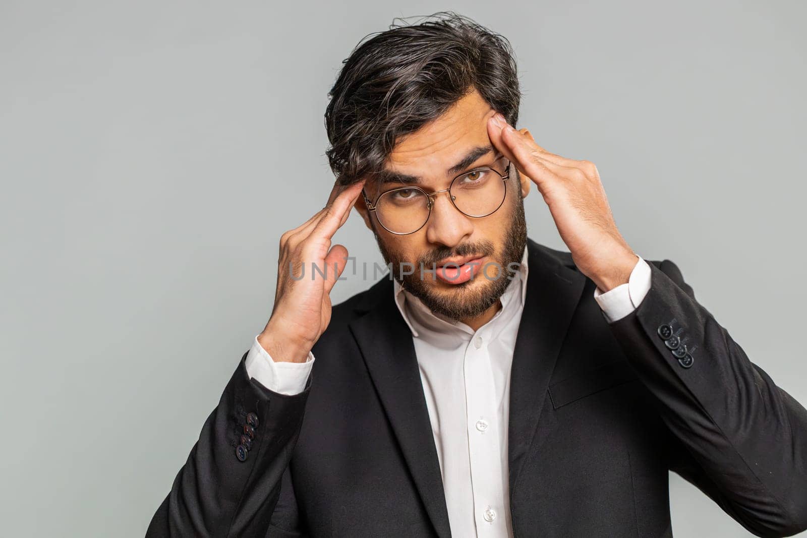 Displeased exhausted Indian business man rubbing temples to cure headache problem, suffering from tension, migraine, stress, grimacing in pain, high blood pressure isolated alone on gray background