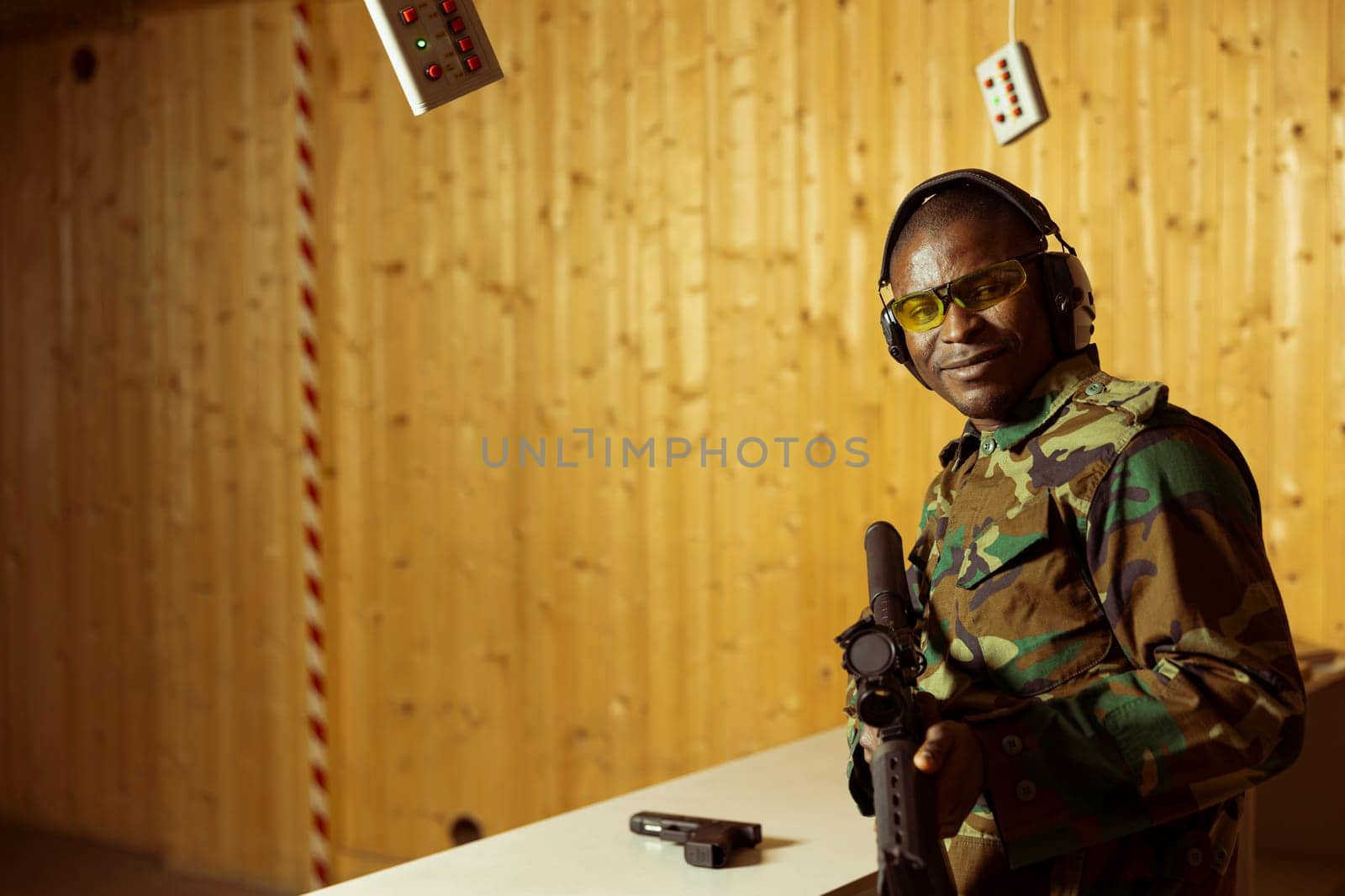 Portrait of smiling soldier in uniform doing training in shooting range, learning to use rifle. Happy military unit in firing range practicing with combat weapons, wearing protective equipment