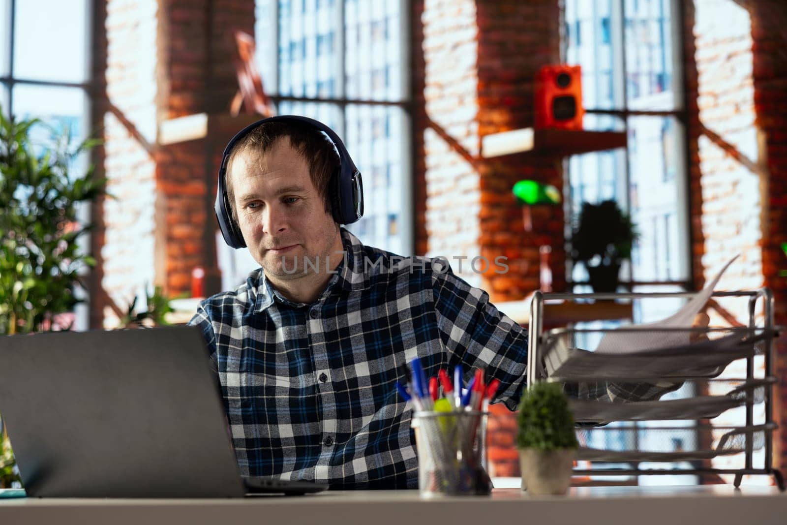 home office worker at desk using laptop, engaging in video call, participating in virtual meeting with colleagues. Man discussing with coworkers during videoconference meeting, using headset