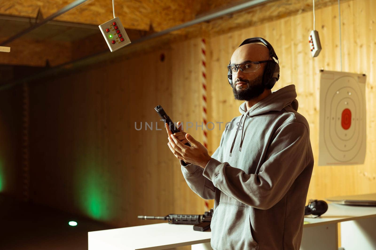 Person wearing safety gear reloading magazine into pistol during firearm practice session at indoor shooting range, learning safety practices. Arab man loading gun, doing self defense preparation