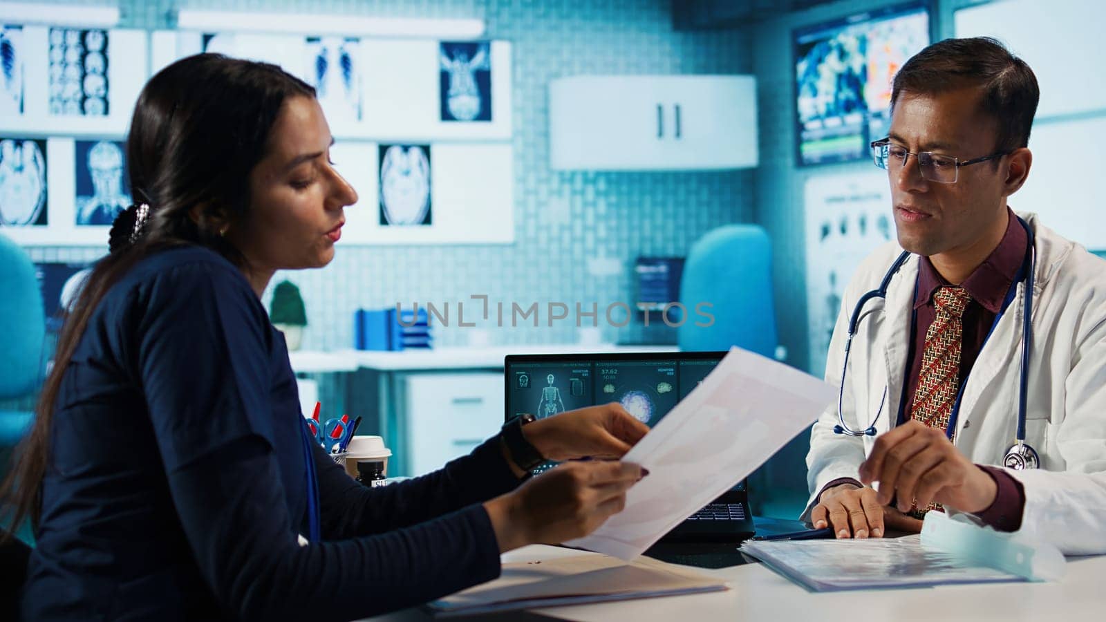 Indian healthcare expert sharing medical expertise with a patient in office, reviewing x ray scans and MRI diagnostics to focus on accurate treatment and recovery. Insurance consultation. Camera B.