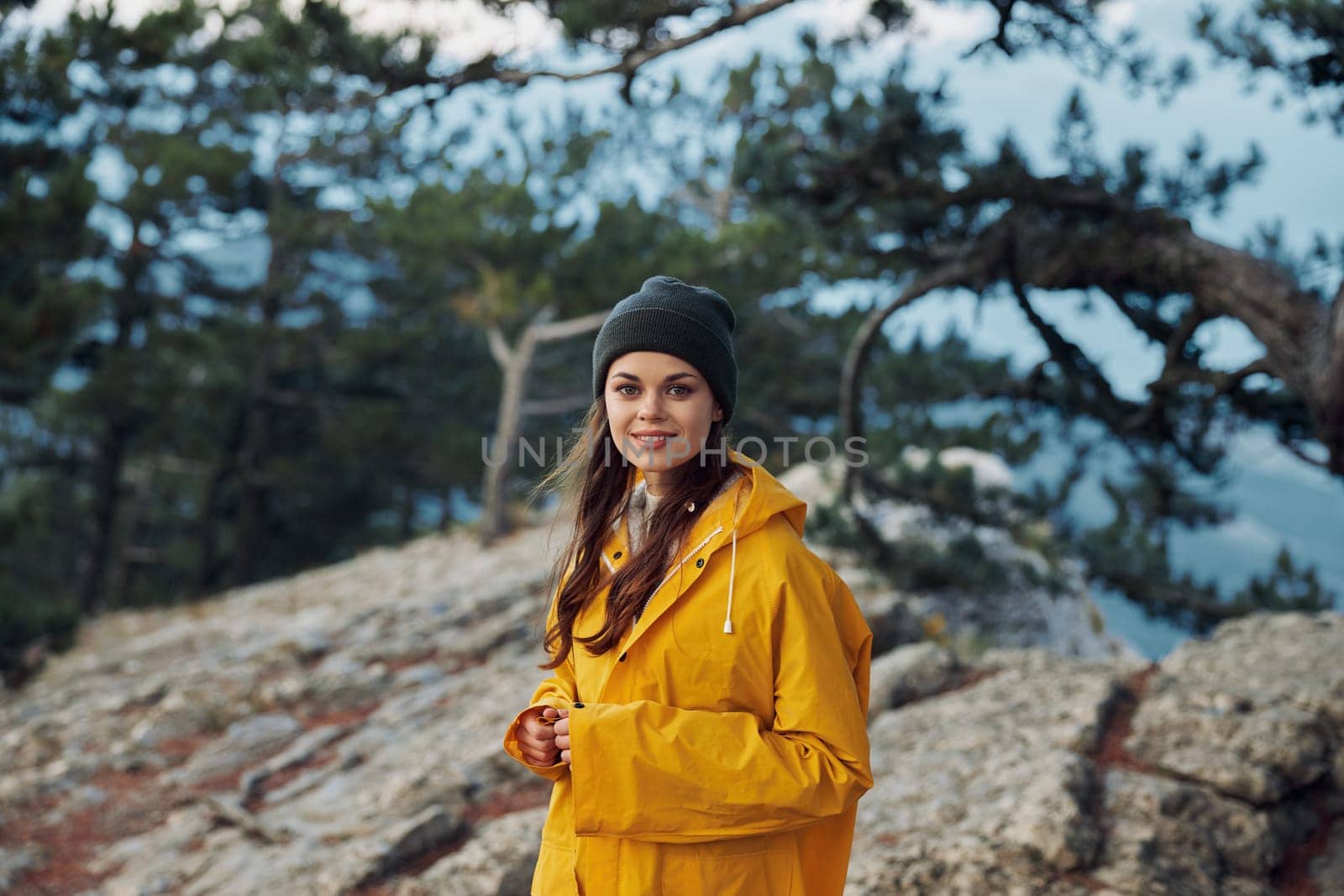 A woman in a yellow raincoat enjoying the breathtaking view from the top of a mountain surrounded by lush trees Travel adventure in nature