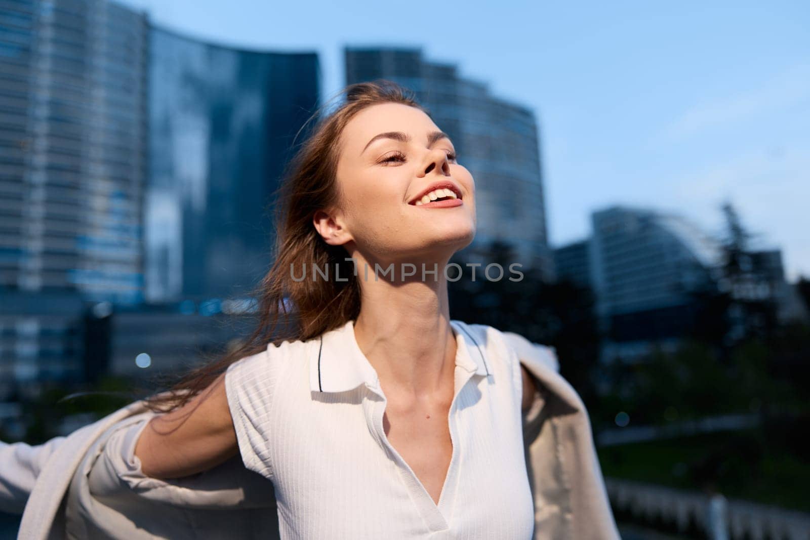 young happy woman wearing white shirt enjoys freedom and success in urban business environment with modern buildings, daylight, and confident energy