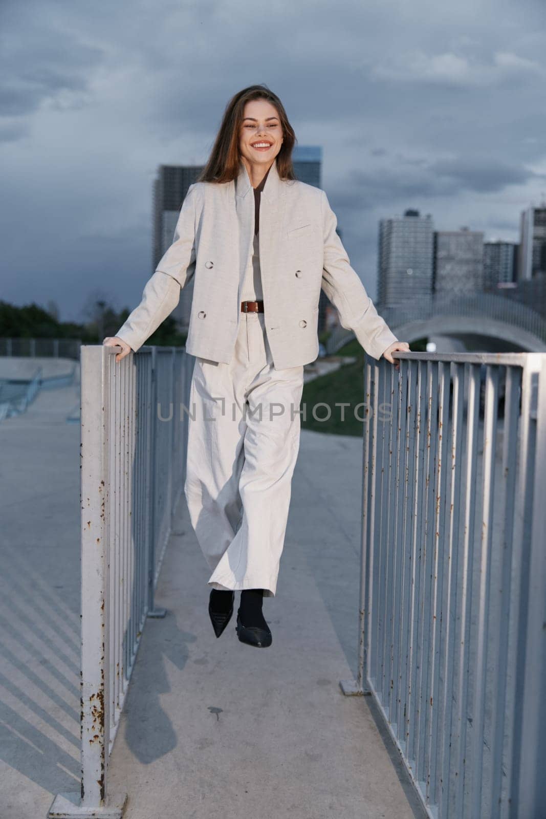 A confident woman dressed in a light-colored business outfit, smiling and posing outdoors against a city skyline, embodies modern professionalism and empowerment.