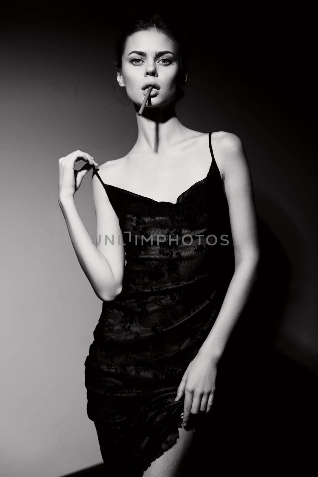 Elegant woman in a fitted black dress posing with a cigarette, exuding confidence and sophistication. The monochrome backdrop enhances the mood of modern fashion photography.