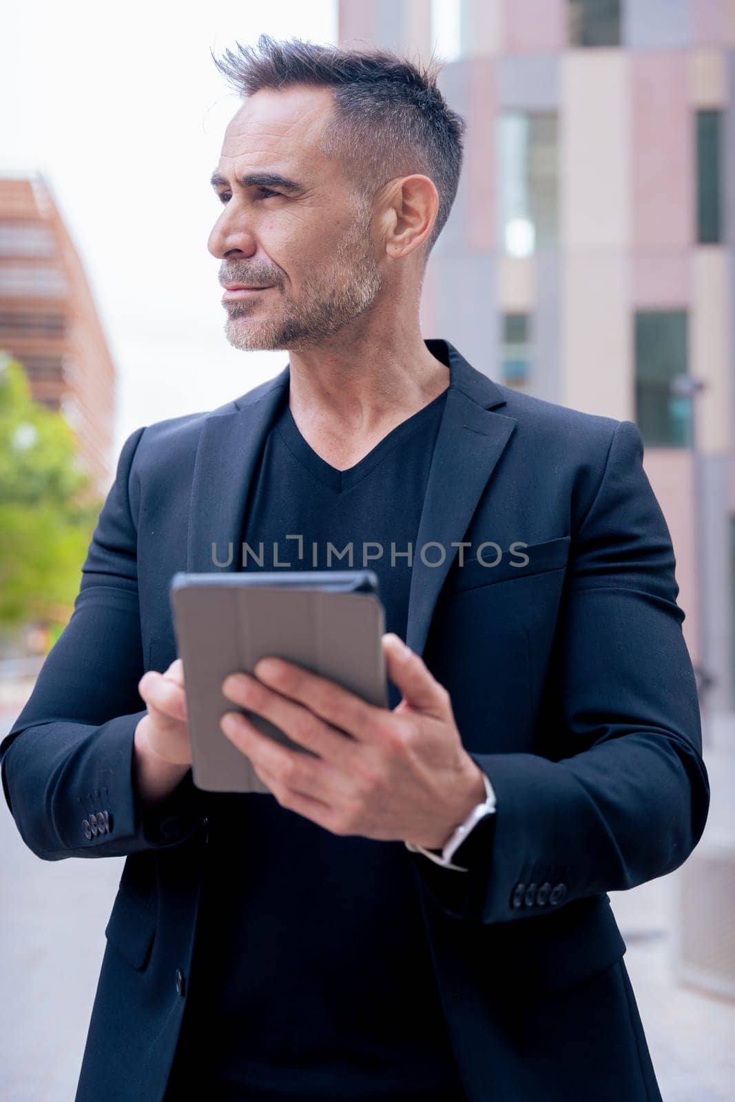 Confident businessman standing outdoors using a tablet in a modern urban setting.He appears focused and professional. Concept of digital work, technology, and contemporary business lifestyle. Vertical