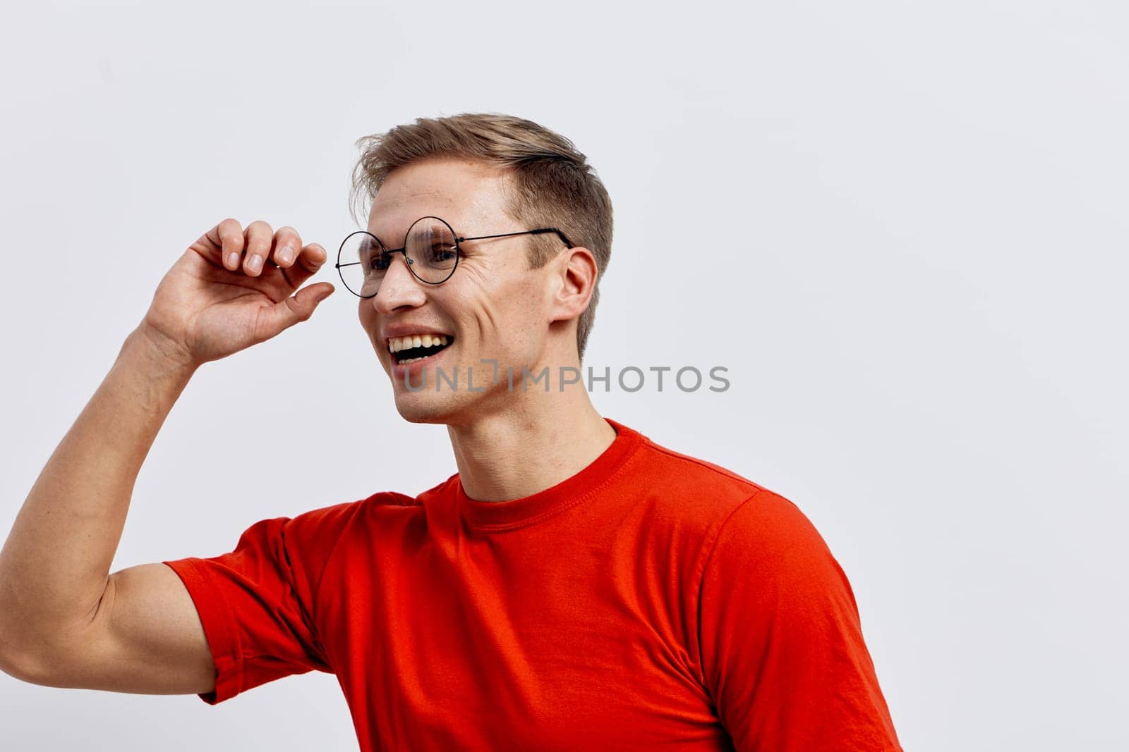 Smiling young caucasian man in red t-shirt wearing round glasses look aside with cheerful mood and positive emotion isolated on white background. Natural casual style photography reflects digital detox and mental health concept.