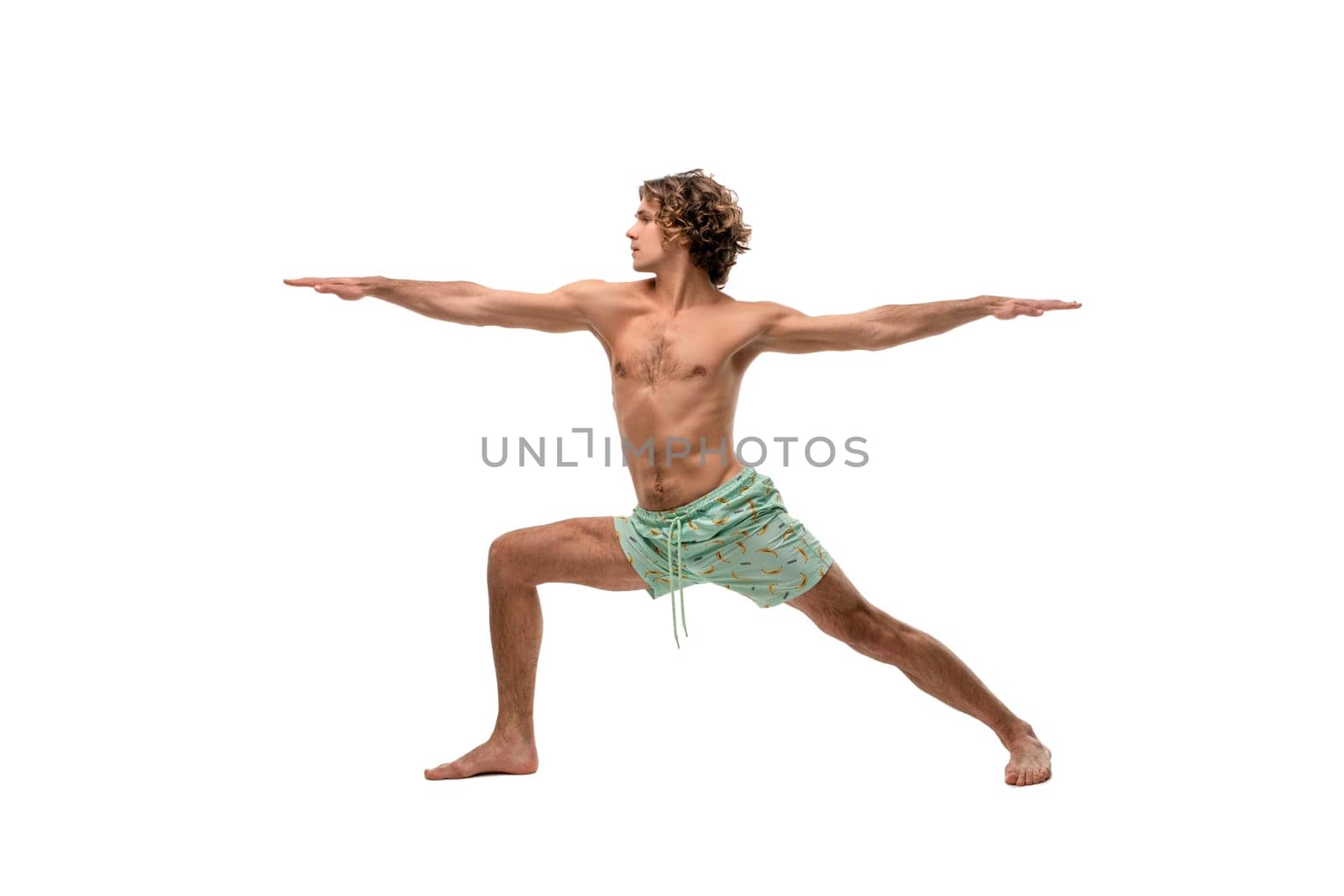 Full body barefoot young male with naked torso spreading arms and doing Virabhadrasana B pose during yoga session isolated