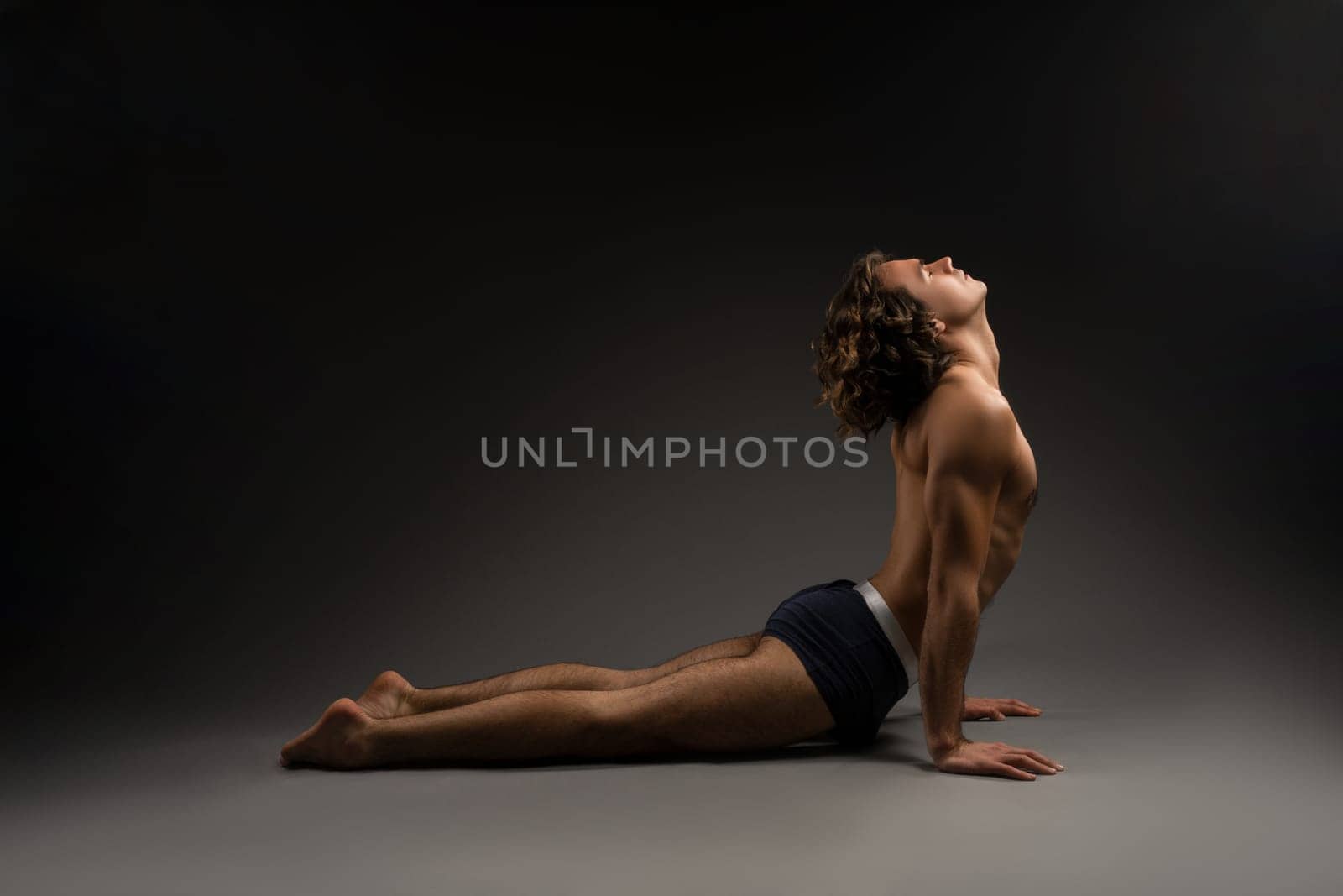 Side view of flexible young male in boxer briefs closing eyes and stretching back in Urdhva Mukha Svanasana pose during yoga session