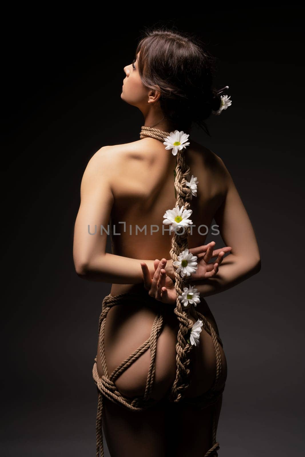 Gentle bdsm with flowers - Back view of anonymous topless female model tied up with ropes with white flowers