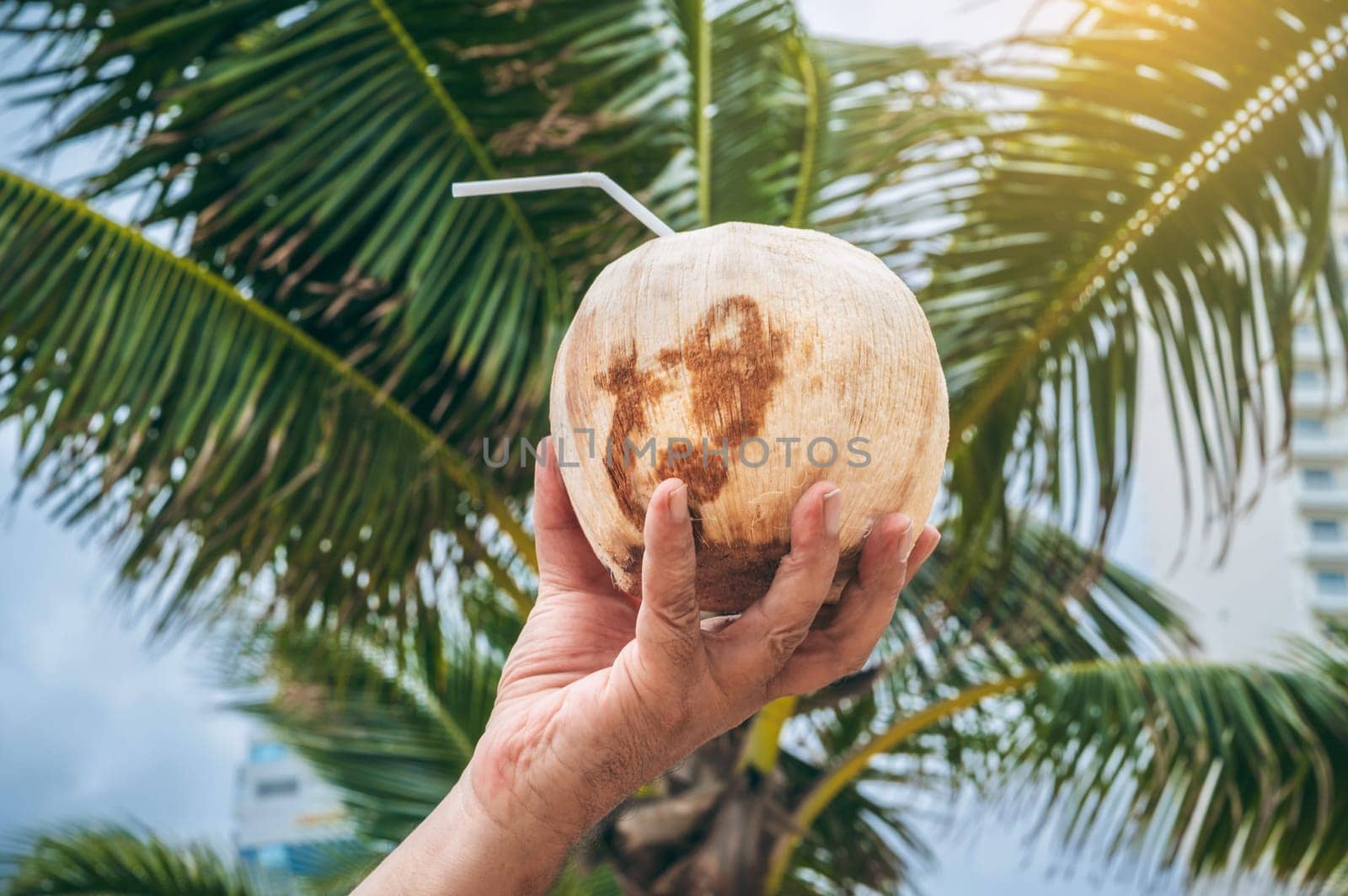 drinking coconut with a straw in a man's hand on the background of palm trees. Concept of traveling and relaxing in a tropical resort on a sunny day