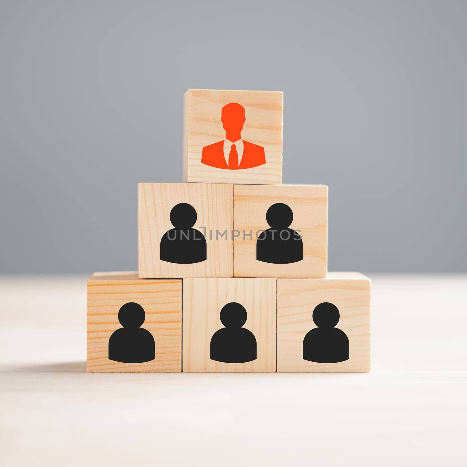 A red manager icon stands out prominently from a group of staff employee icons printed on a wooden block, representing the concept of different thinking and human development within a business setting