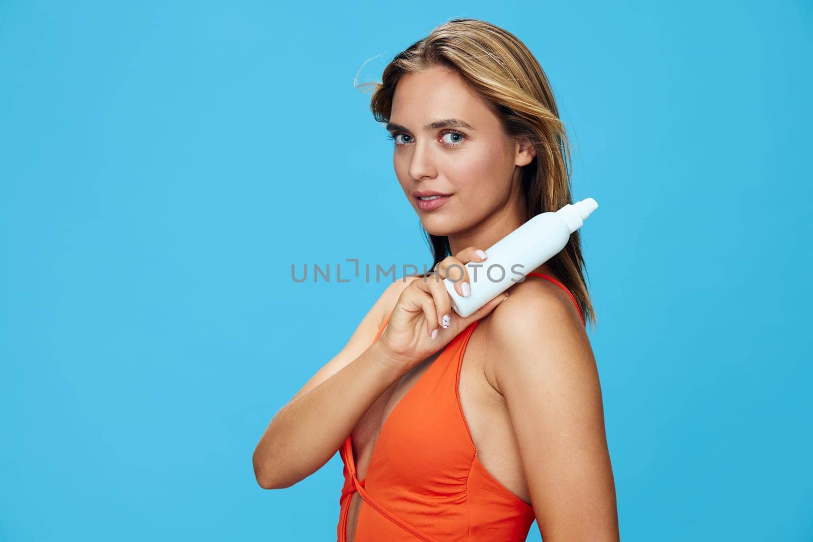 Vibrant woman in orange swimsuit holding hair dryer against serene blue background