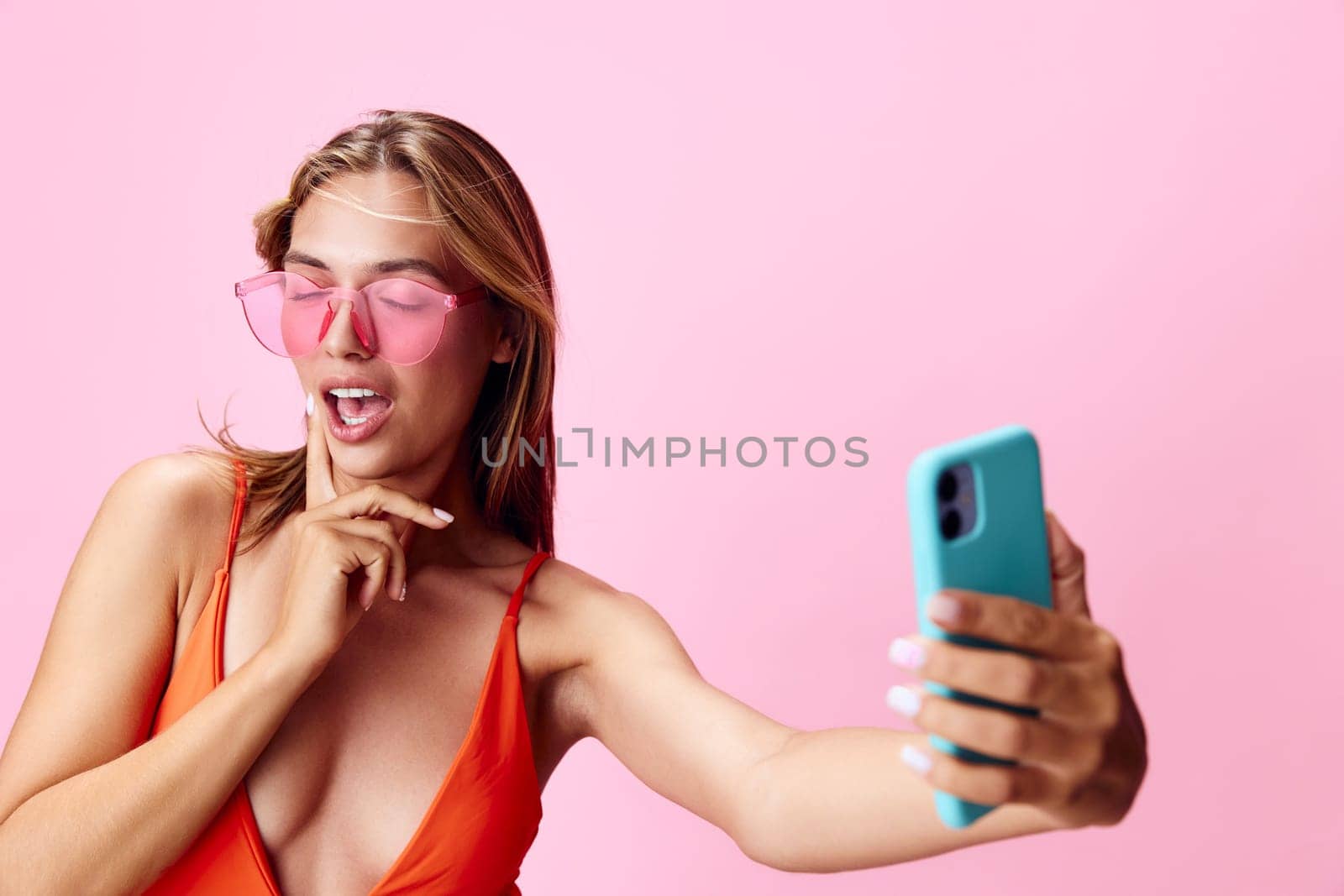 Vibrant and fun a young woman in a swimsuit capturing the perfect selfie moment on a pink background